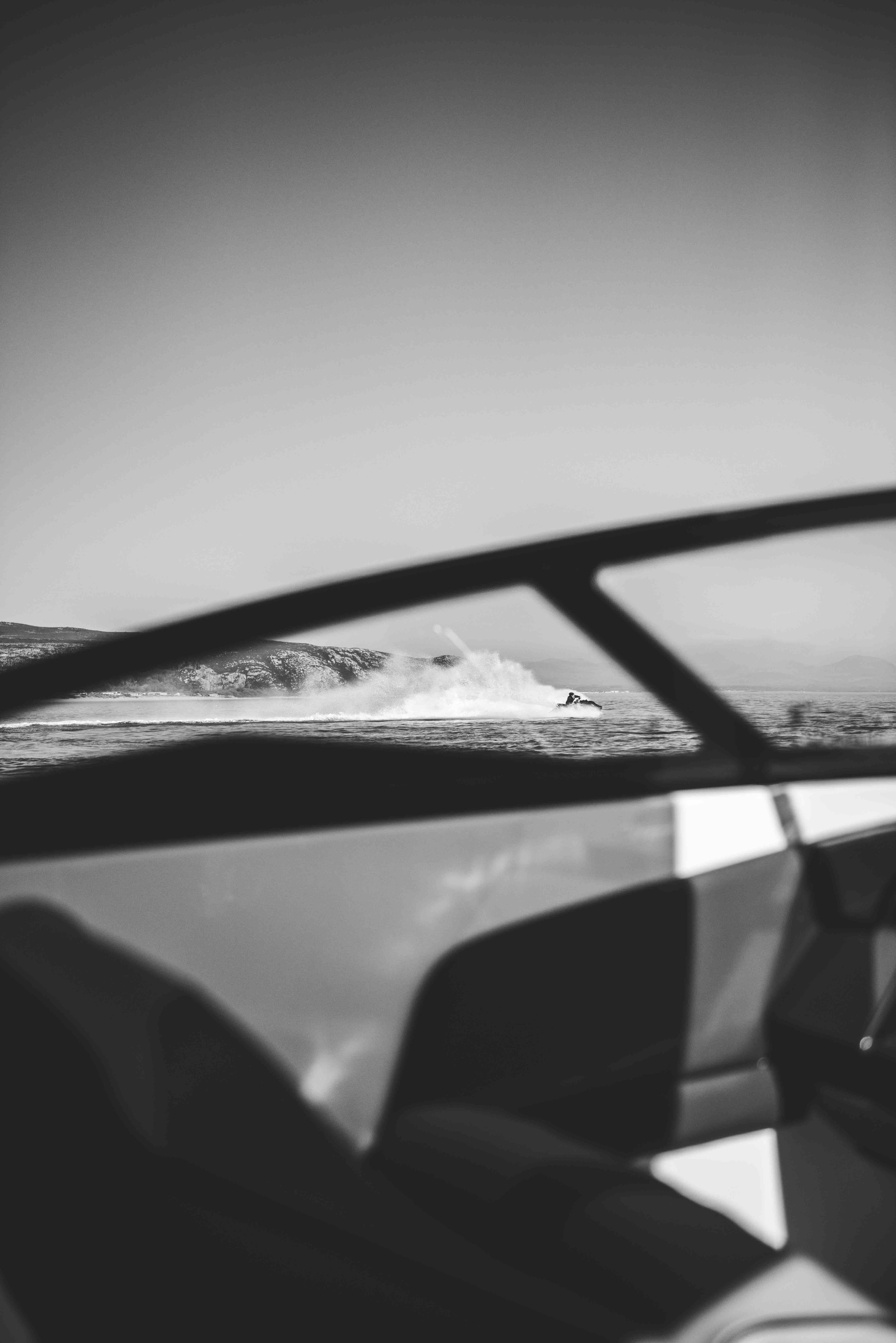 Black and white photo of a jet ski on water, viewed through the frame of a speedboat.
