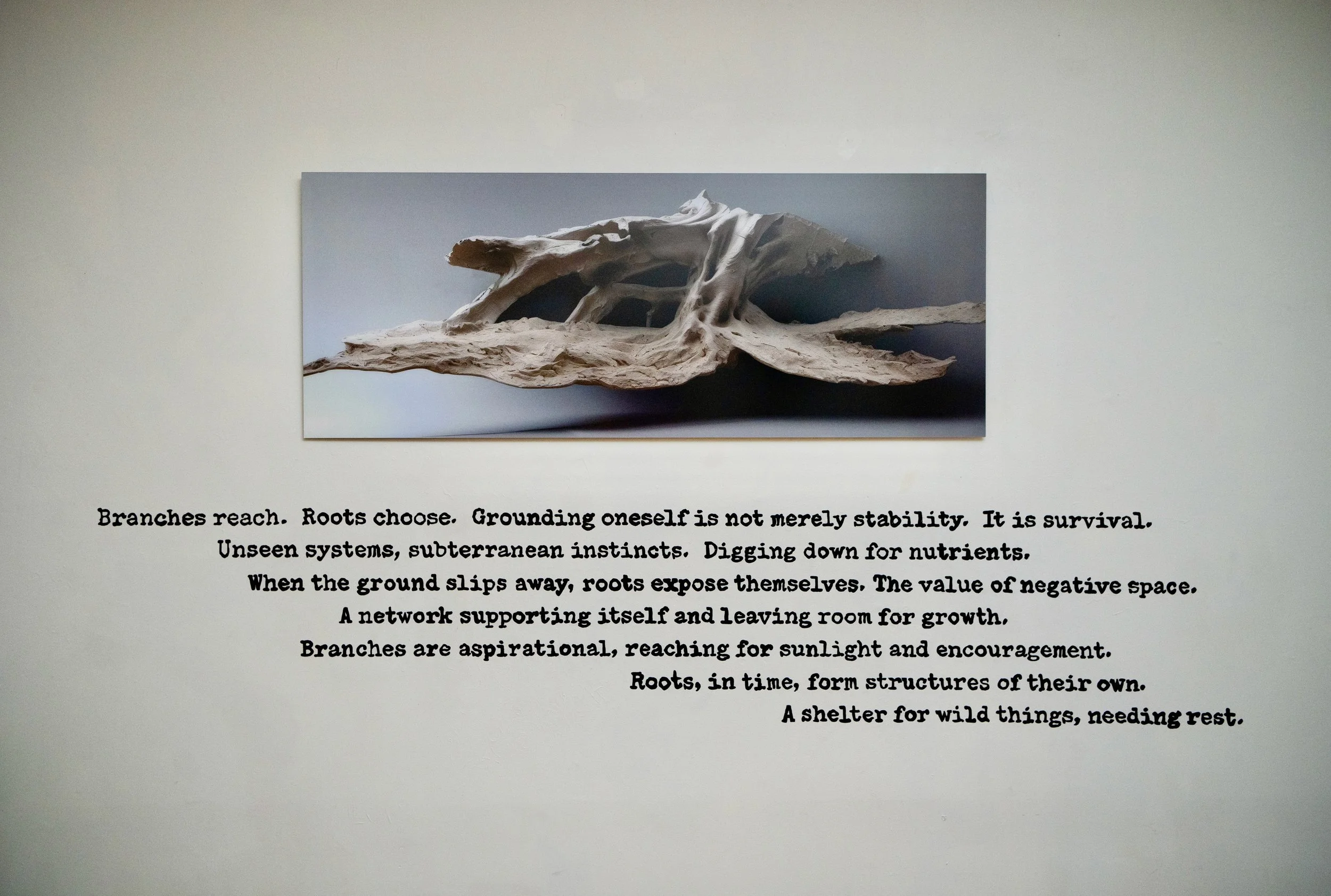 Gallery installation of artwork titled Roots with a wall painting of poetry in typewriter font hand painted
