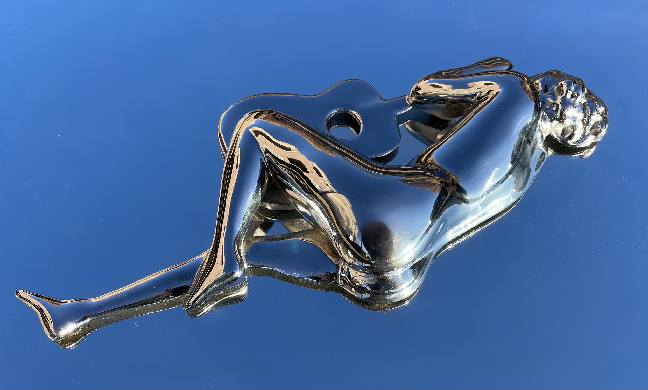 Liquid metal silver sculpture of a nude woman lying down with a guitar