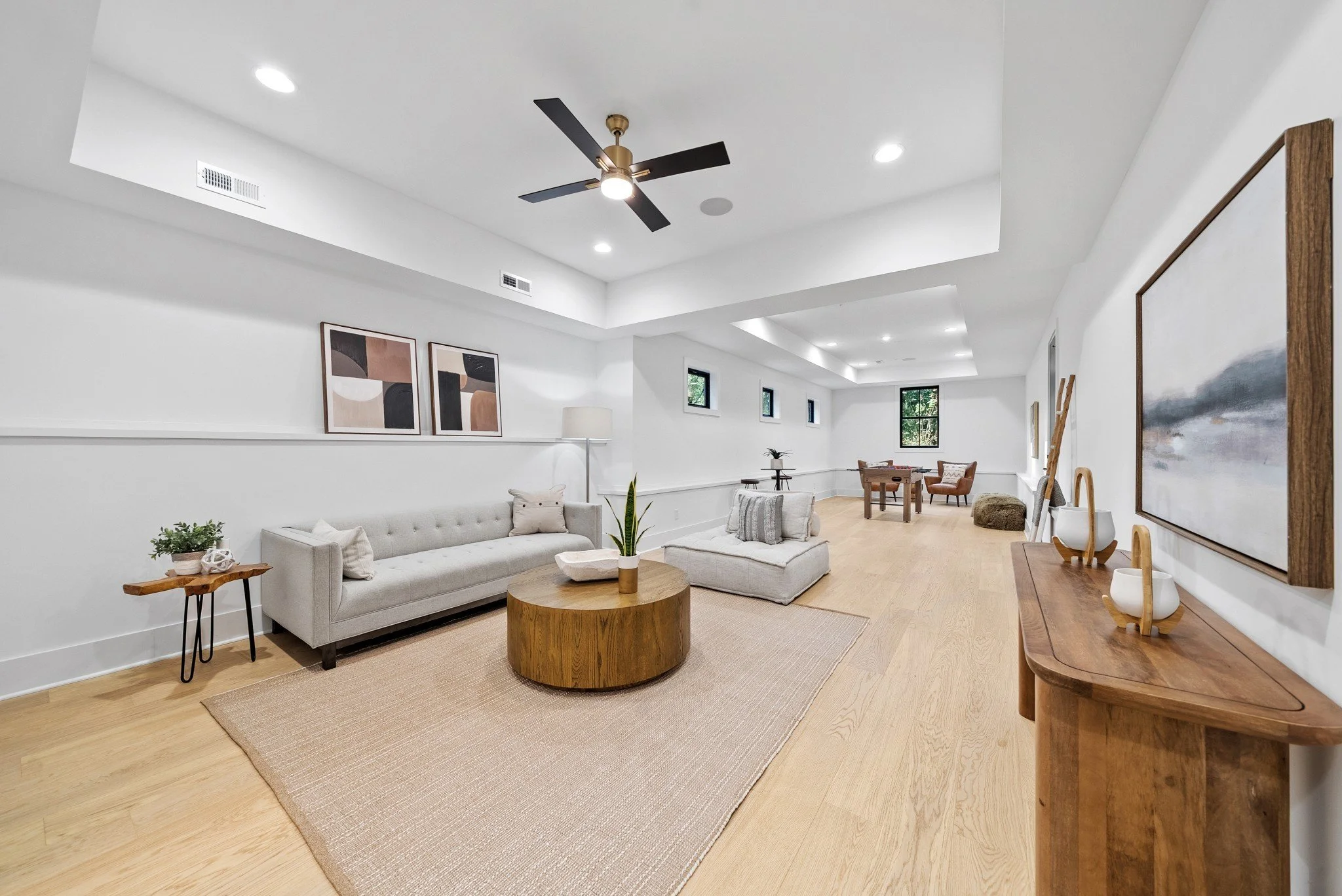 Spacious, modern living room with white walls, wooden flooring, gray sofa, coffee table, abstract wall art, and decorative items.