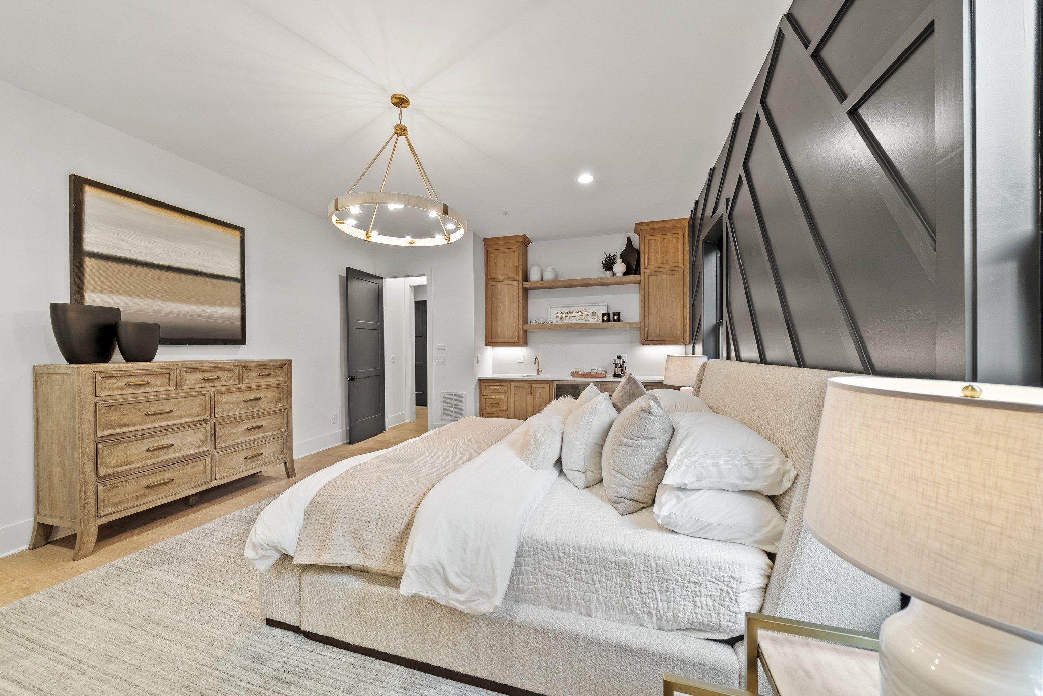 Modern bedroom with a beige bed, black accent wall, wooden dresser, and pendant light