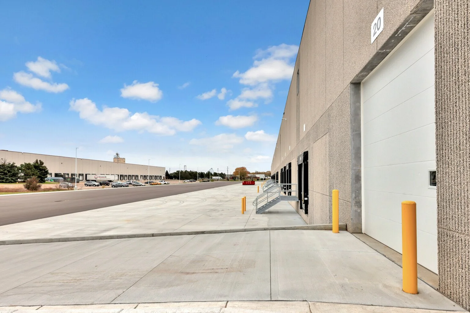 Empty loading dock area with yellow safety posts in front of large warehouse building, clear blue sky above.