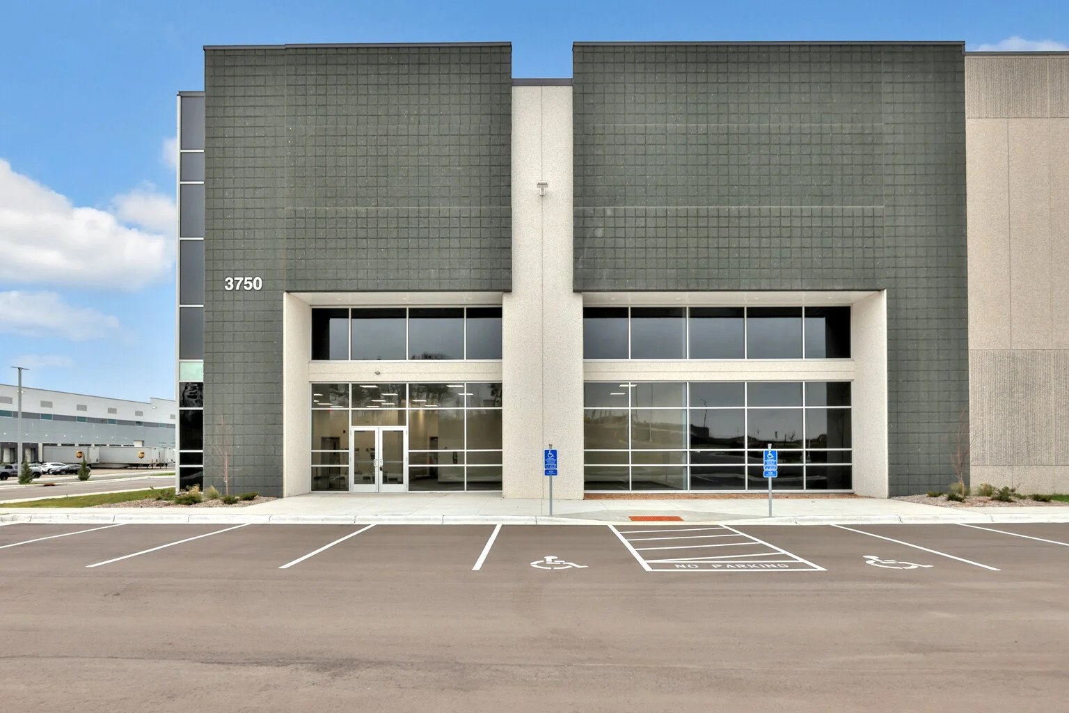 Modern commercial building with the number 3750 on the left side, featuring a glass entrance and multiple parking spaces, including accessible parking spots in the front.