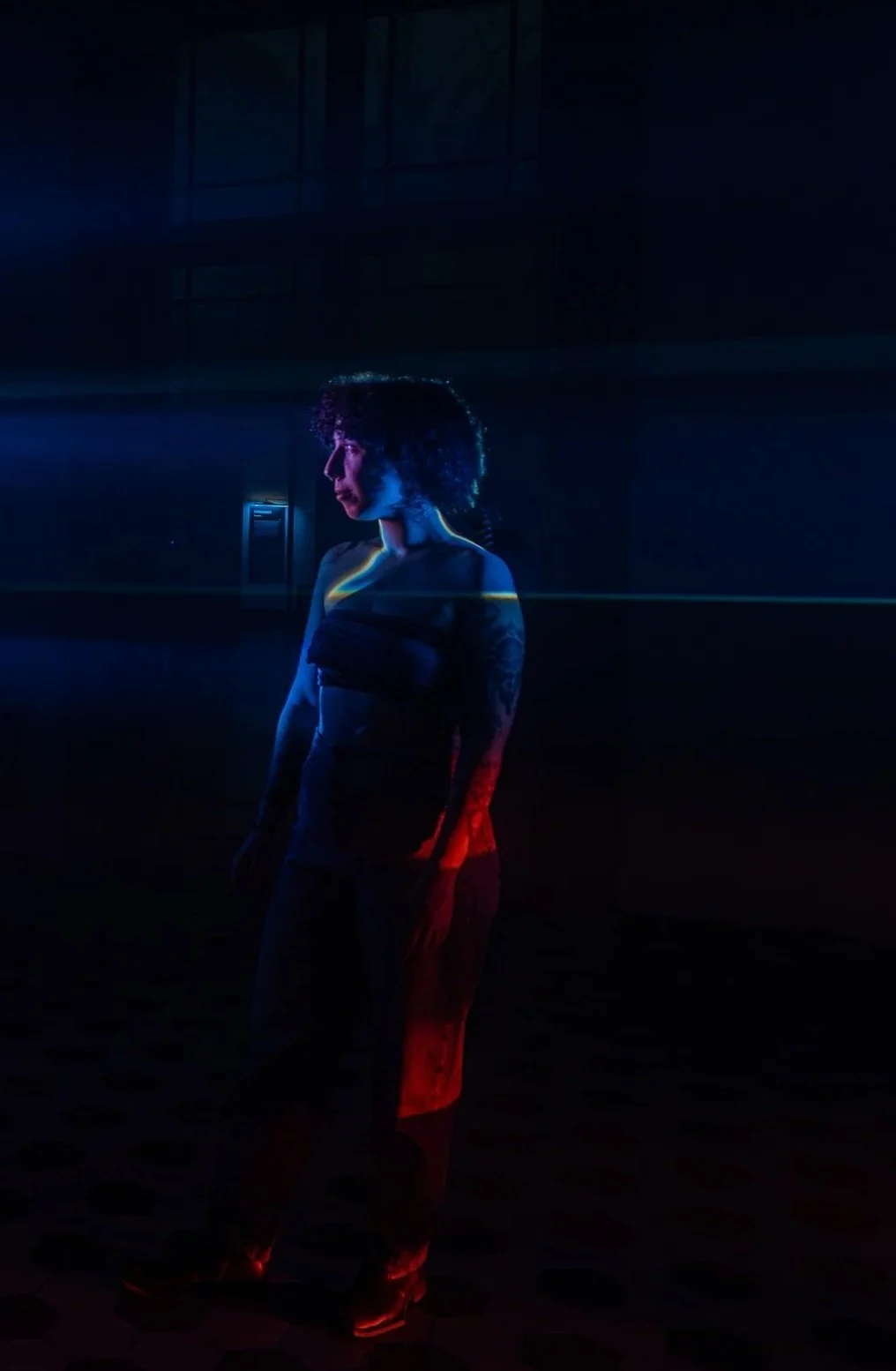 A woman standing in a dark, illuminated environment with dramatic red and blue lighting.