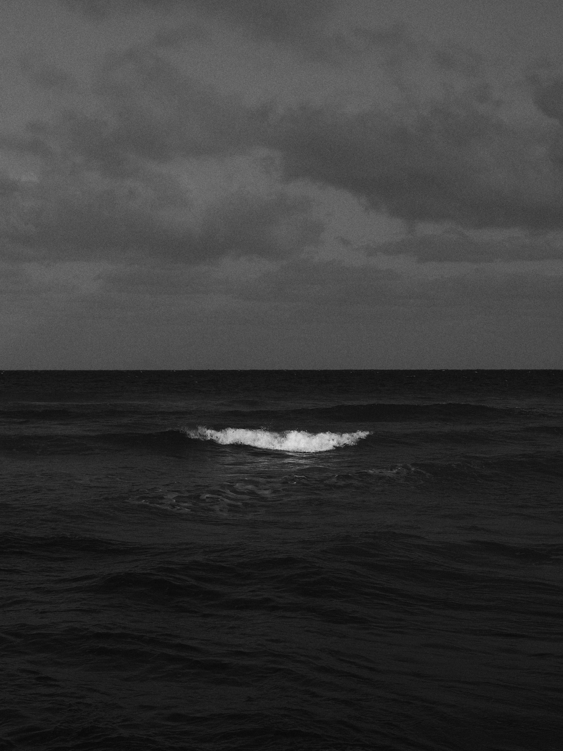 Black and white photo of ocean waves under a cloudy sky.