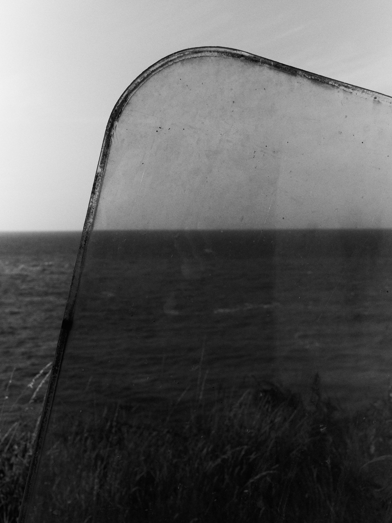 Close-up of a curved, weathered surfboard or similar object with an ocean in the background, captured in black and white.
