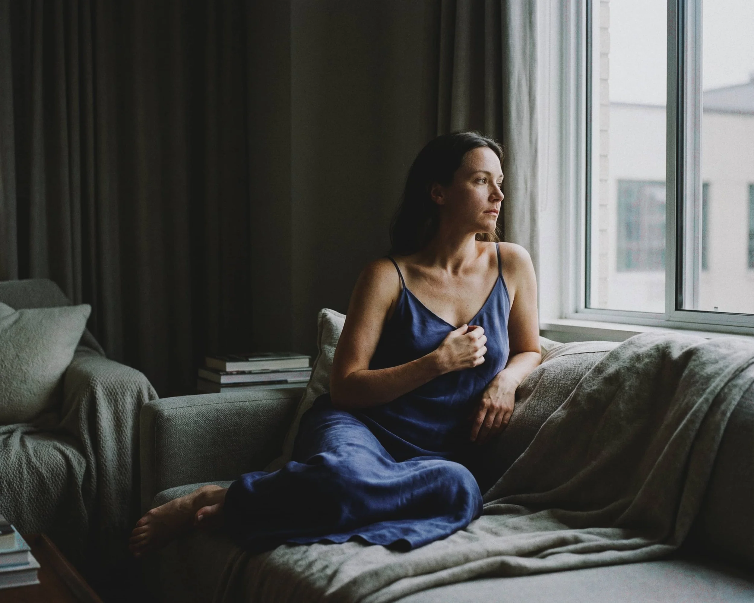 Mujer sentado en un sillón mirando por la ventana, con expresión pensativa