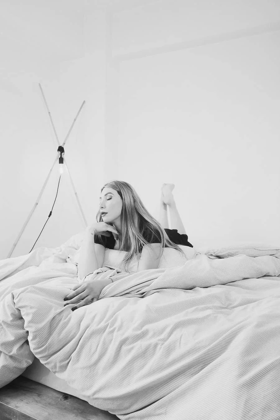 Mujer recostada en la cama en una habitación con paredes blancas y lámpara de pie