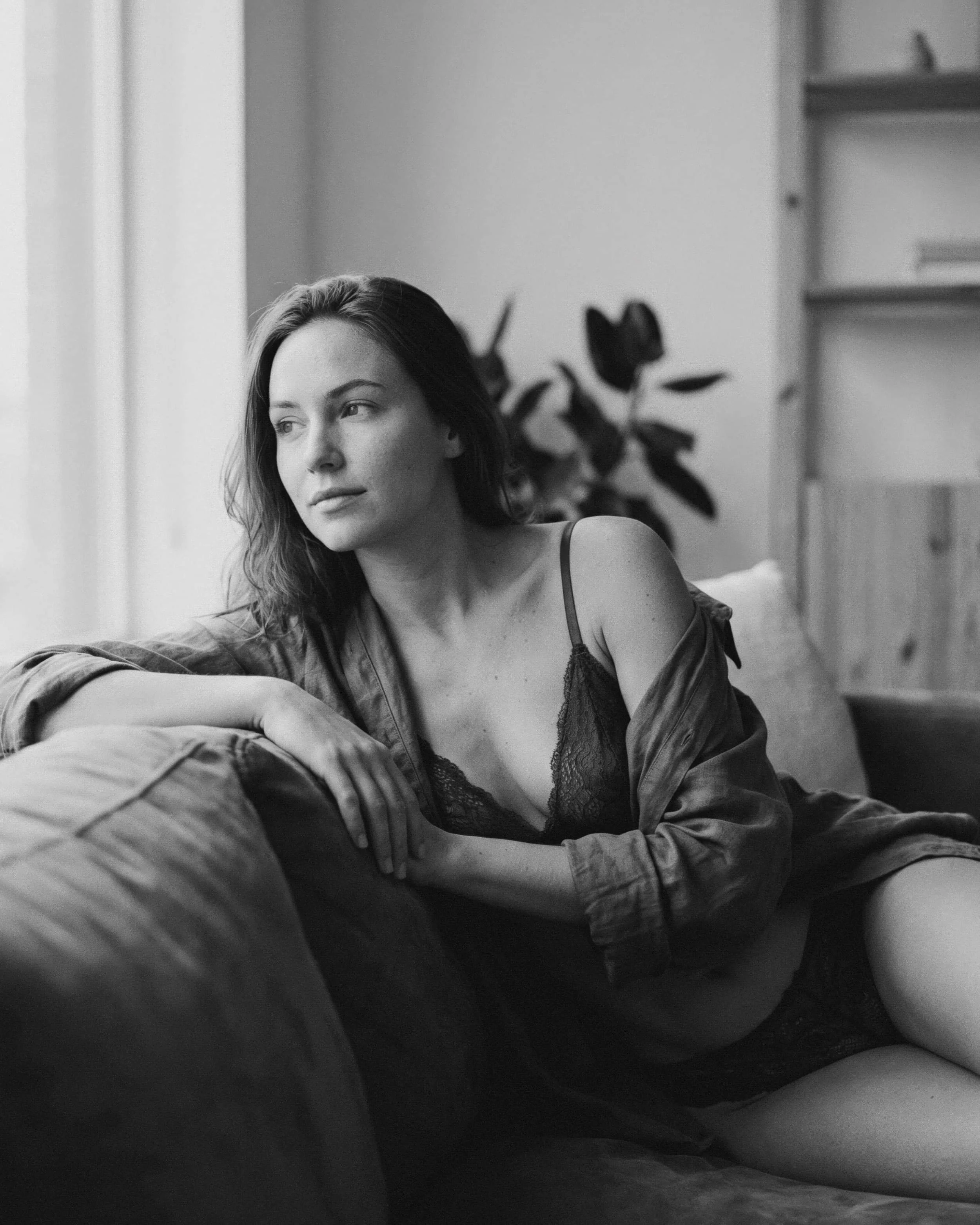 Retrato en blanco y negro de una mujer joven sentada en un sofá, mirando hacia la ventana, usando ropa de dormir