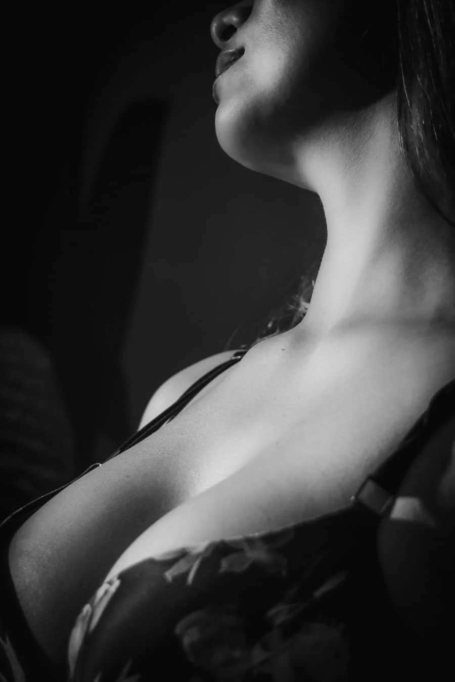 Retrato en blanco y negro de una mujer vista desde el cuello hacia arriba, con énfasis en su cuello y clavícula, con sombra y luz suave.