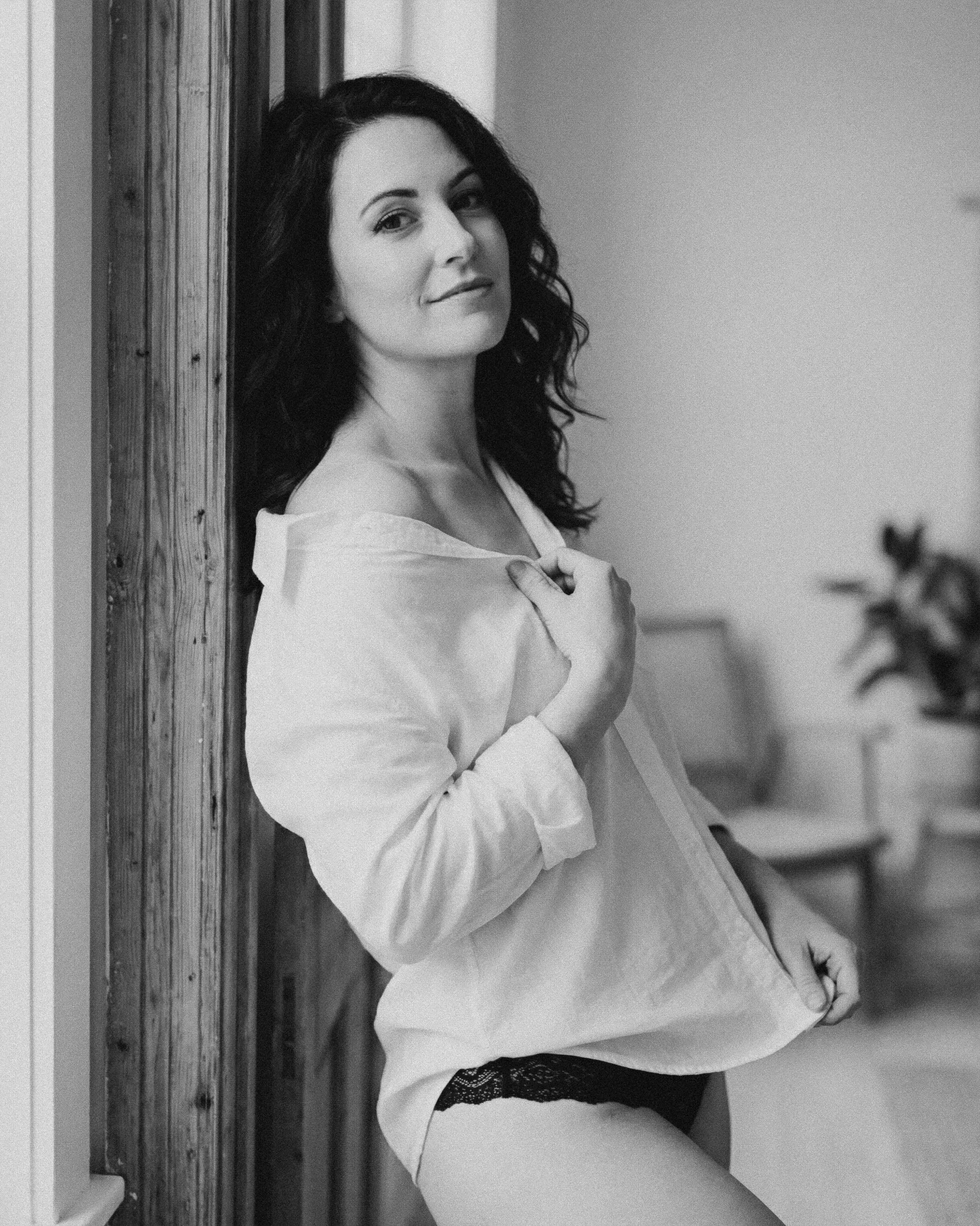 Mujer posando con camisa blanca y pantalones cortos de encaje, sonriendo en un espacio interior.