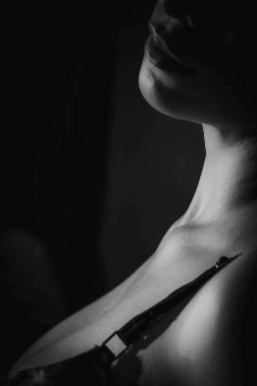 Vista en negro y blanco del perfil de una persona con gafas, enfocando en la barbilla y el cuello, con iluminación suave y sombra en la cara.