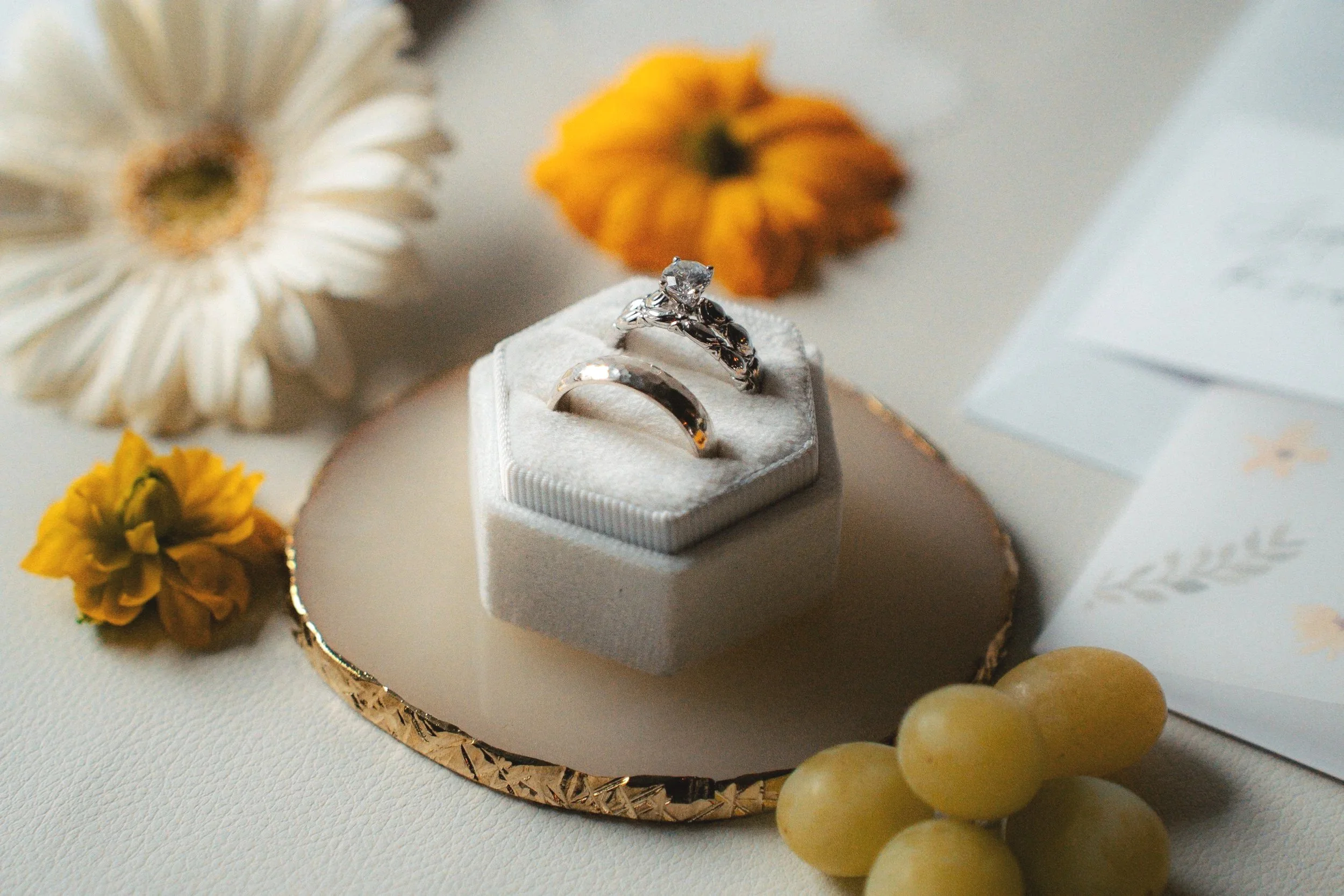 Silver rings in a jewelry box surrounded by flowers, grapes, and a white decorative object