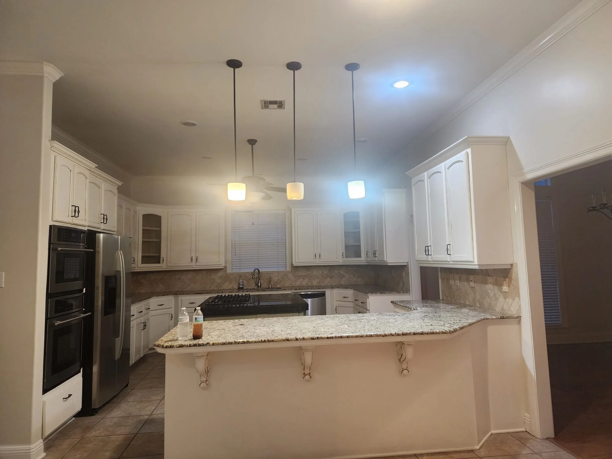 Modern kitchen with white cabinets, granite countertops, stainless steel appliances, and pendant lighting.