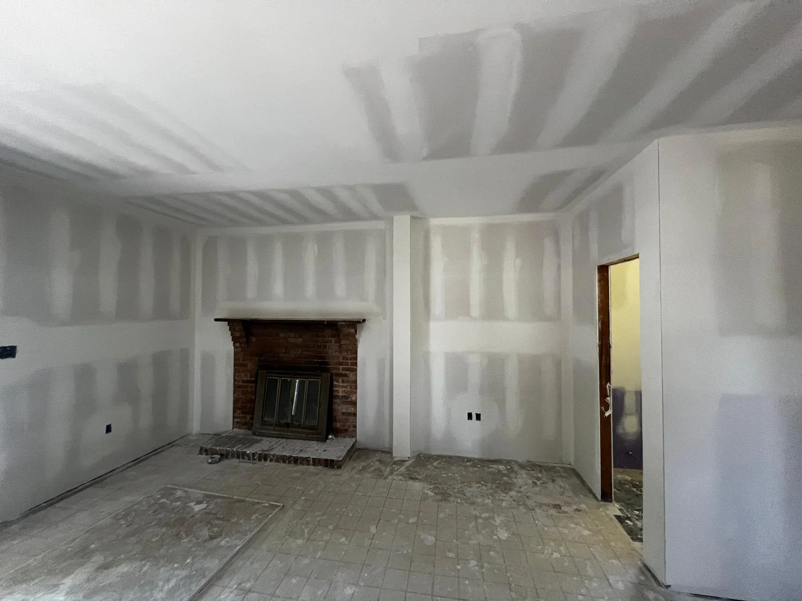 Room with unfinished drywall, brick fireplace, and unfinished floor.