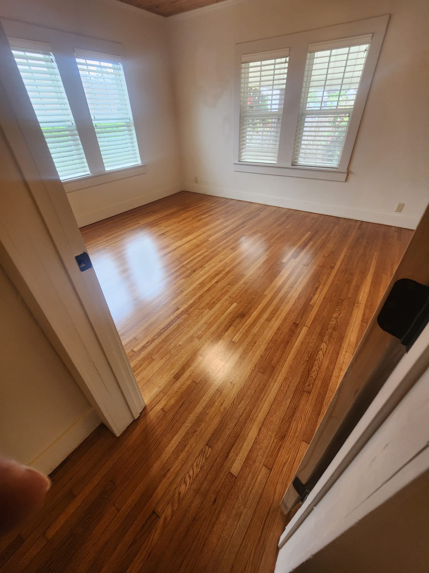 Empty room with hardwood floors and two windows with white blinds.