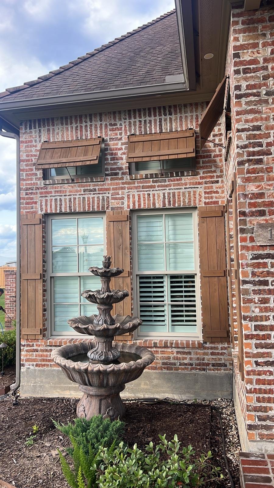 Brick house exterior with wooden shutters and a multi-tiered stone water fountain in the garden.