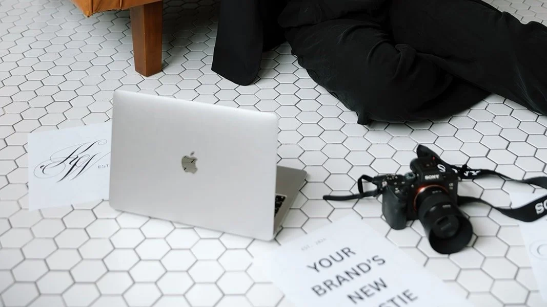 Laptop on hexagonal tile floor with camera and printed sheets.