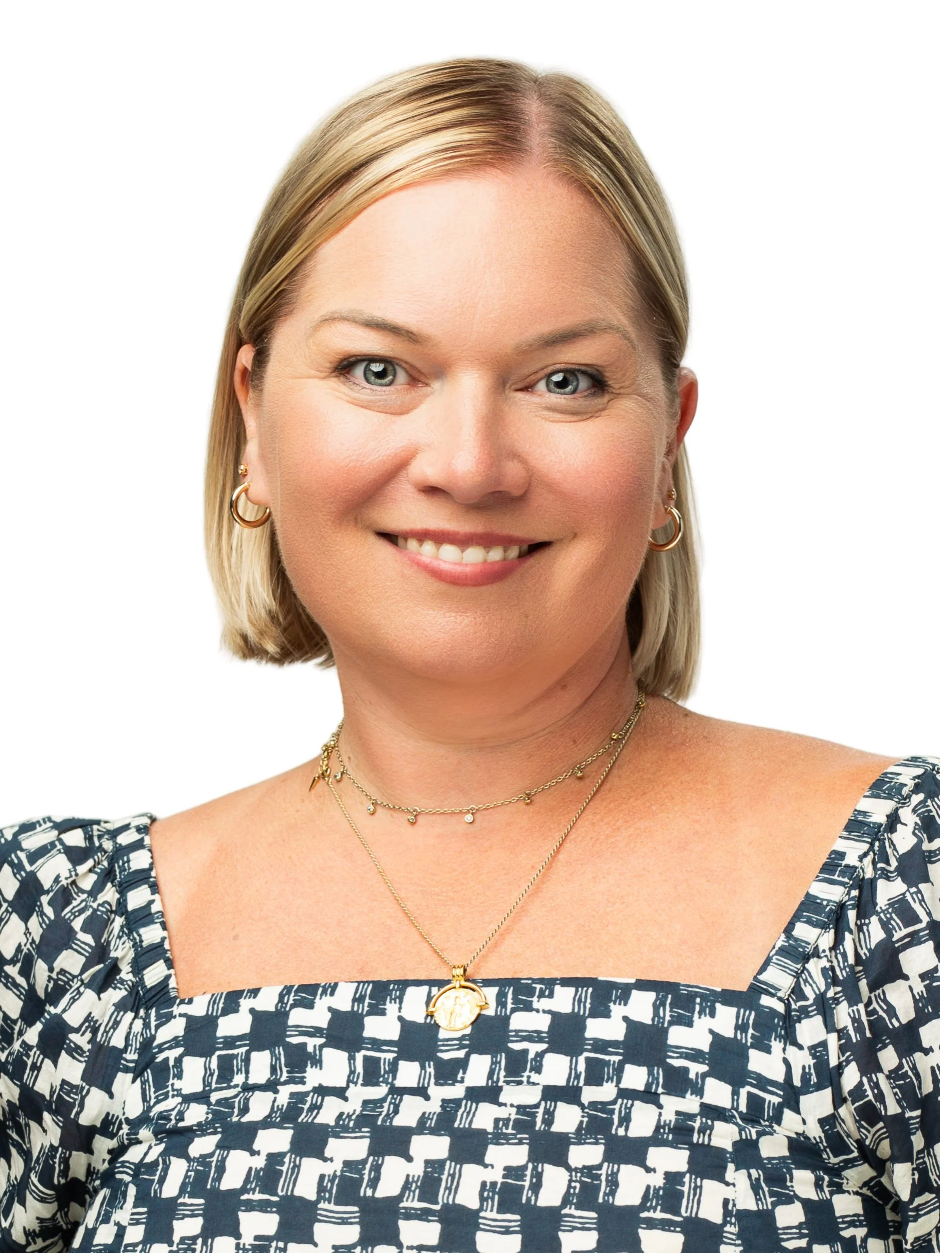 Close-up of a smiling woman with blonde hair, wearing gold hoop earrings, layered gold necklaces, and a patterned navy and white top.