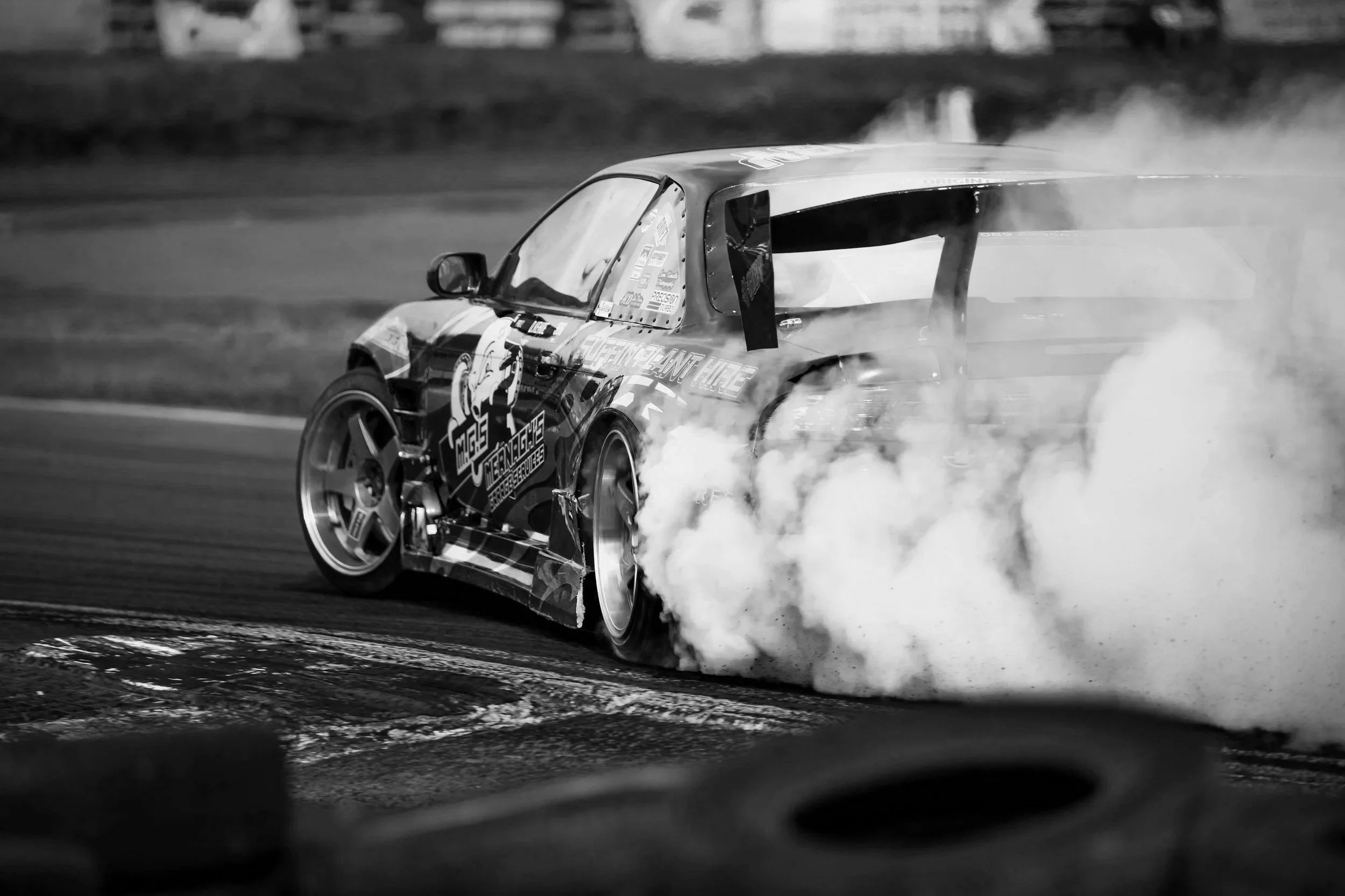 A race car drifting around a corner, producing a large plume of smoke from its tires, on a race track.
