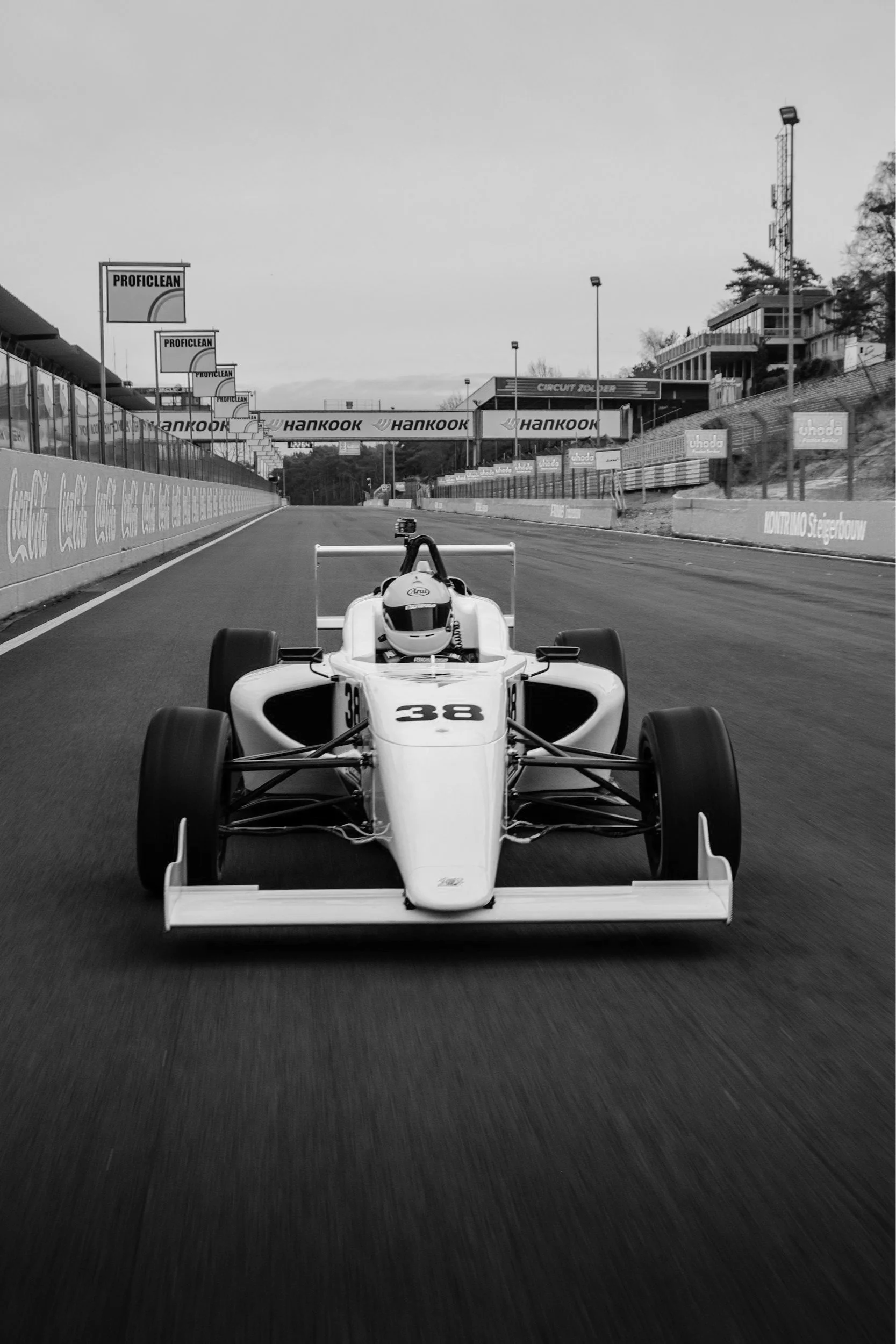A race car on a track, viewed from the front, in black and white.