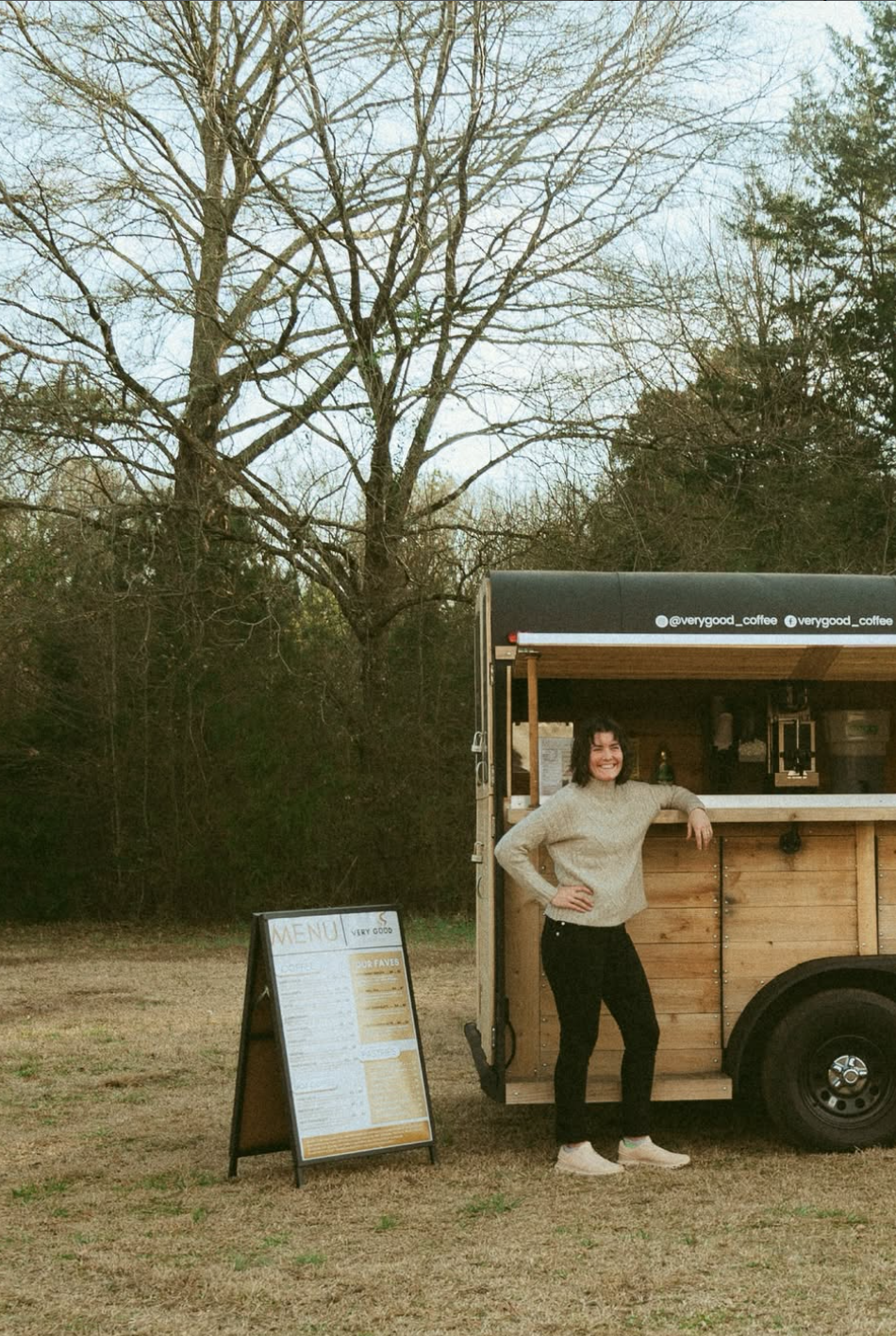 Miriam Arnold, owner of Very Good Coffee, standing confidently in front of her matte black and natural wood mobile coffee trailer serving weddings and events in Georgia
