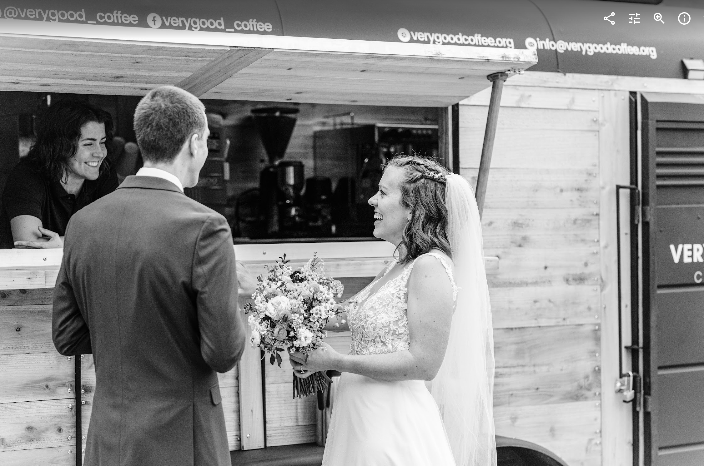 A bride and groom exchanging wedding vows inside a wooden structure while a woman smiles at them, holding a bouquet of flowers.