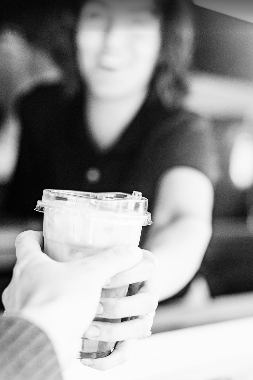 Person handing over a coffee cup with a lid to another person, in black and white.