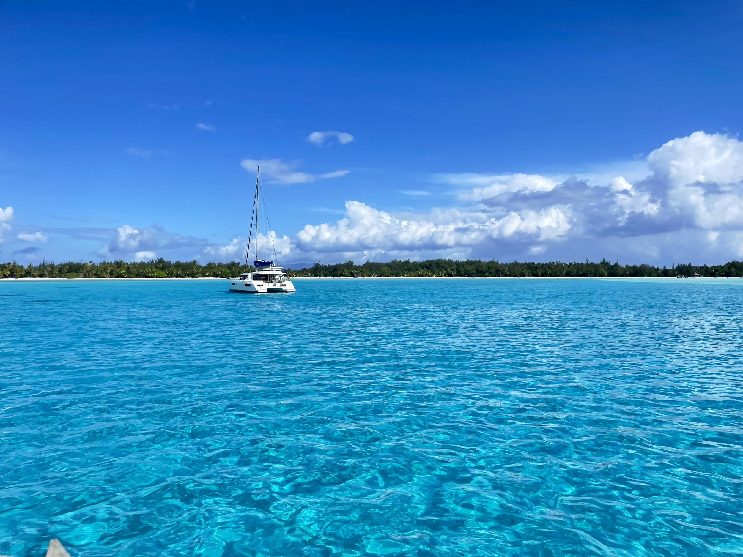 Sailboat on turquoise ocean near lush island under blue sky with clouds.