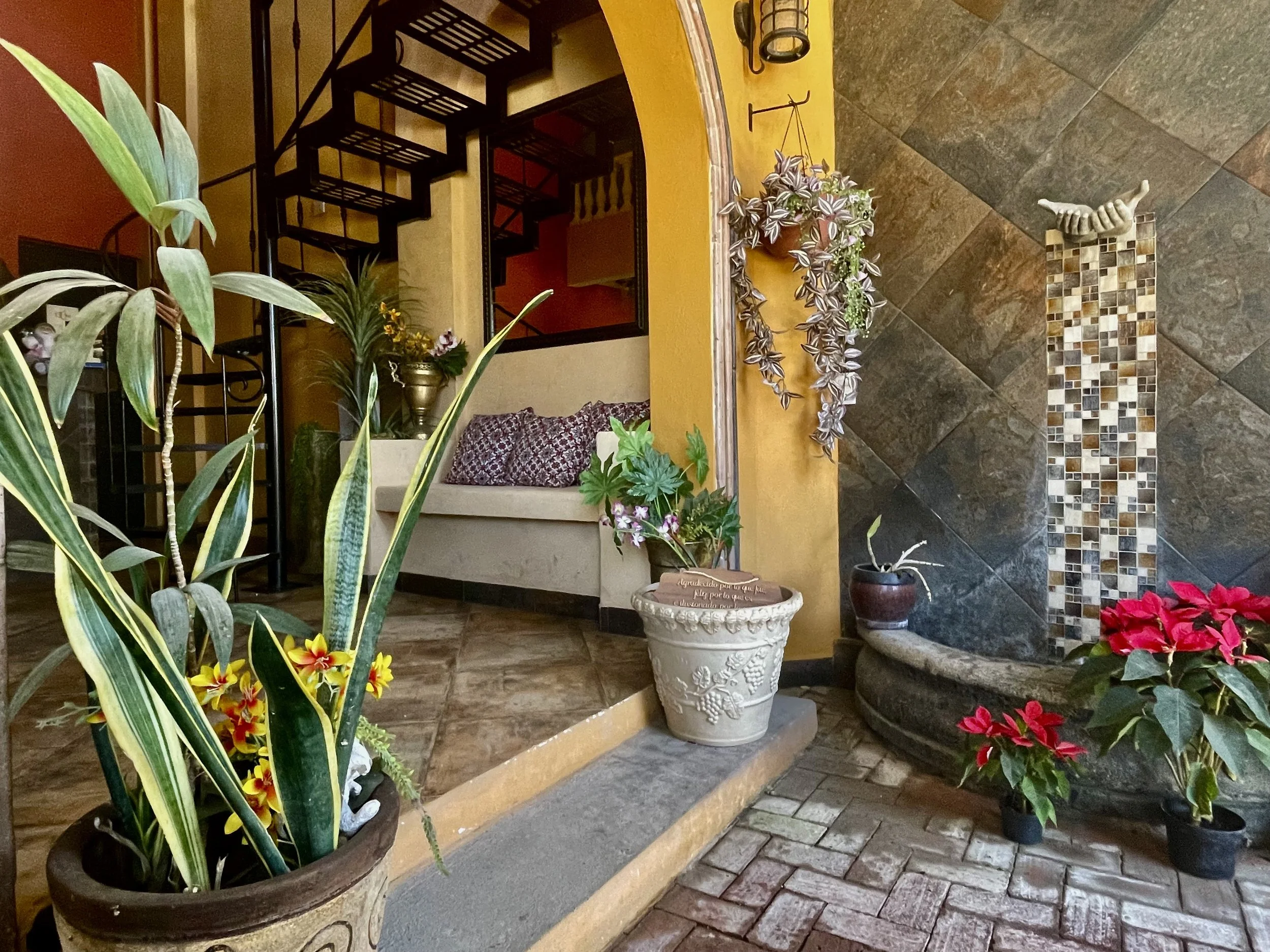 Indoor seating area with a decorative wall and staircase, surrounded by potted plants and flowers.