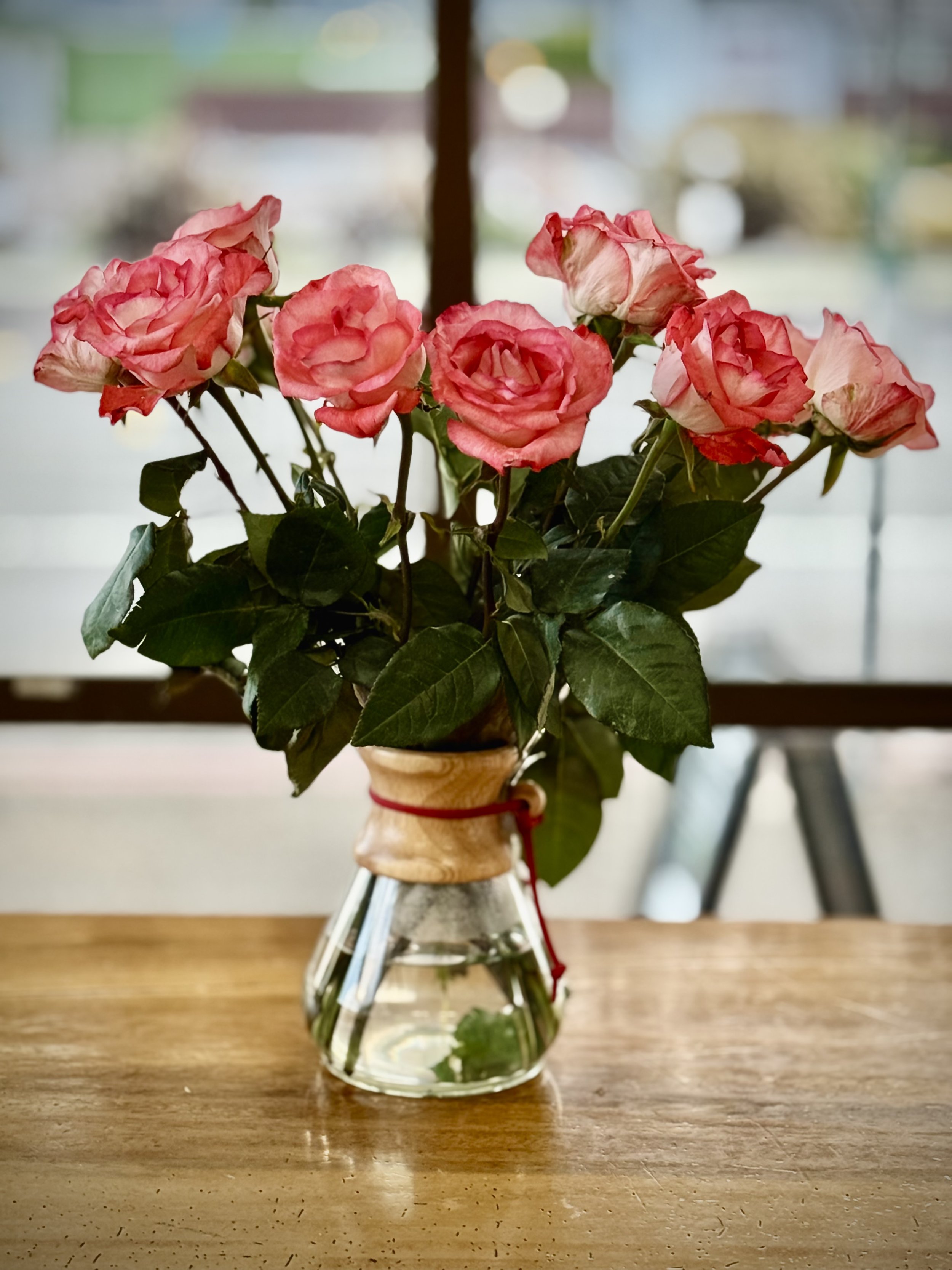 Bouquet of pink roses in a glass vase on a wooden table.