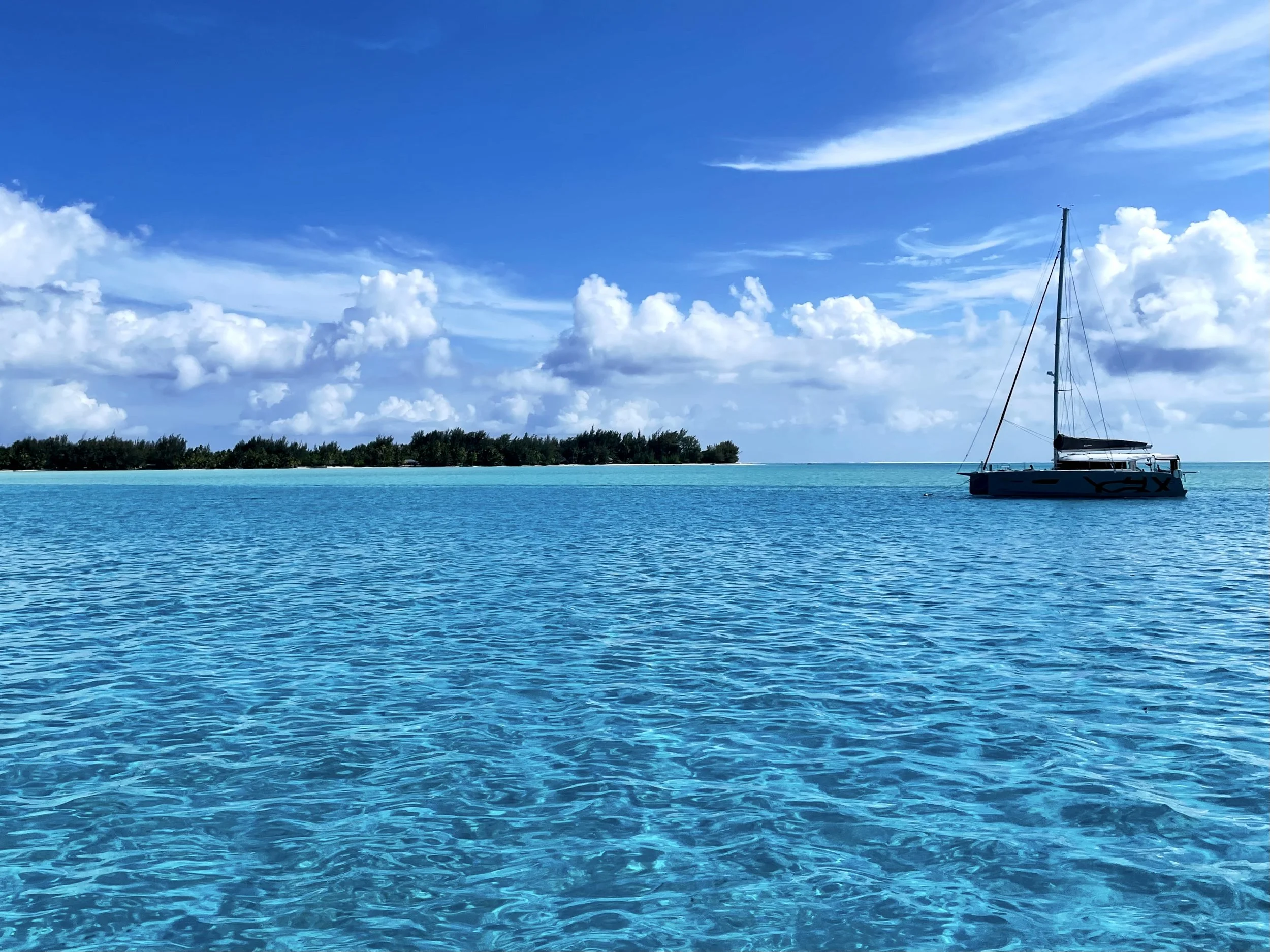 Sailboat on turquoise ocean with distant island and clouds under a blue sky.