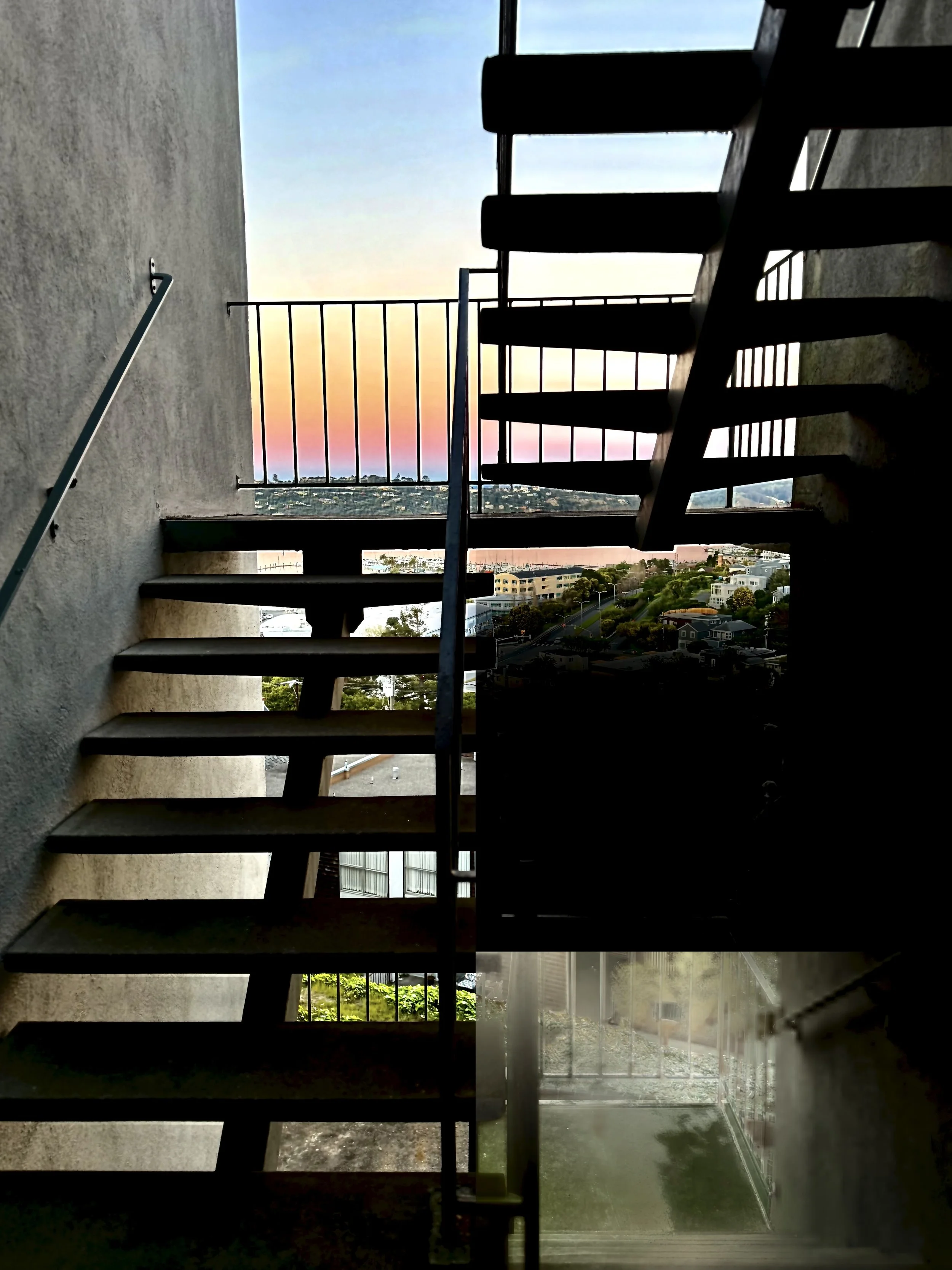 Silhouette of an exterior staircase with a view of a colorful sunset sky and distant cityscape.