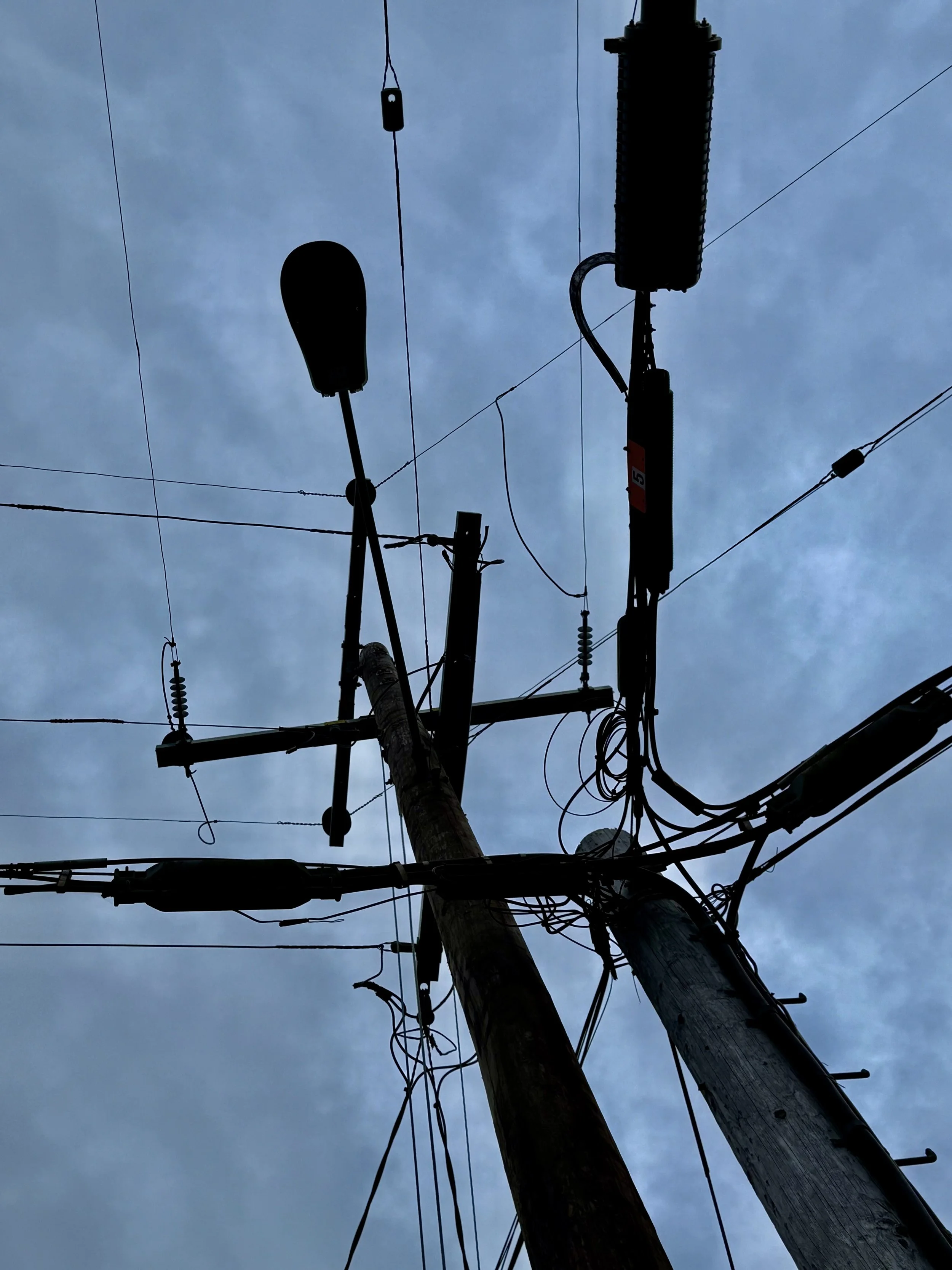 Utility pole with electrical wires and a streetlight silhouette against a cloudy sky.