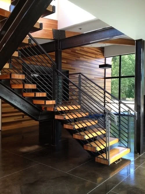 Modern indoor staircase with wooden steps, black metal railings, and glass window letting in natural light, wood-paneled wall background.