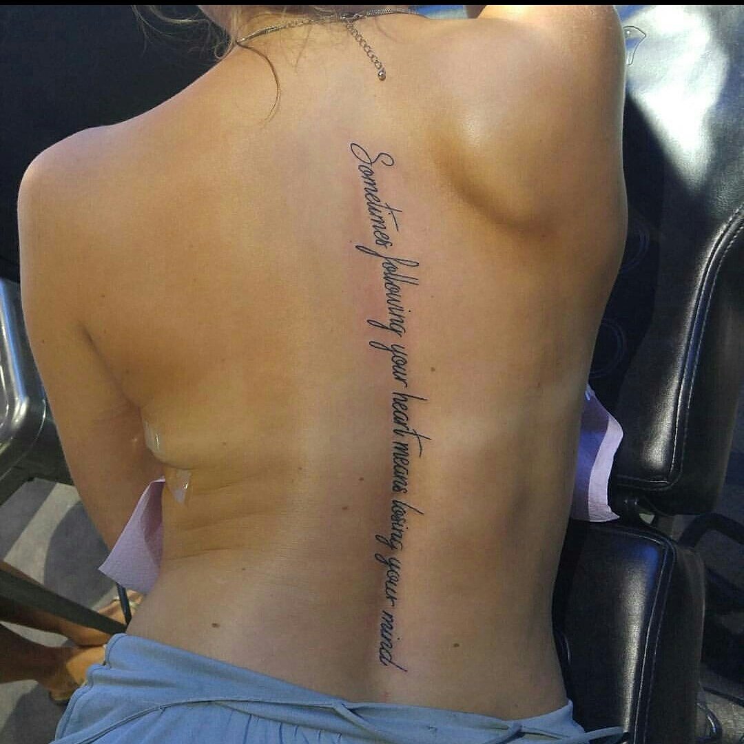 Back tattoo with cursive quote reading, "Sometimes following your heart means losing your mind." Person is lying on their stomach in a tattoo studio.