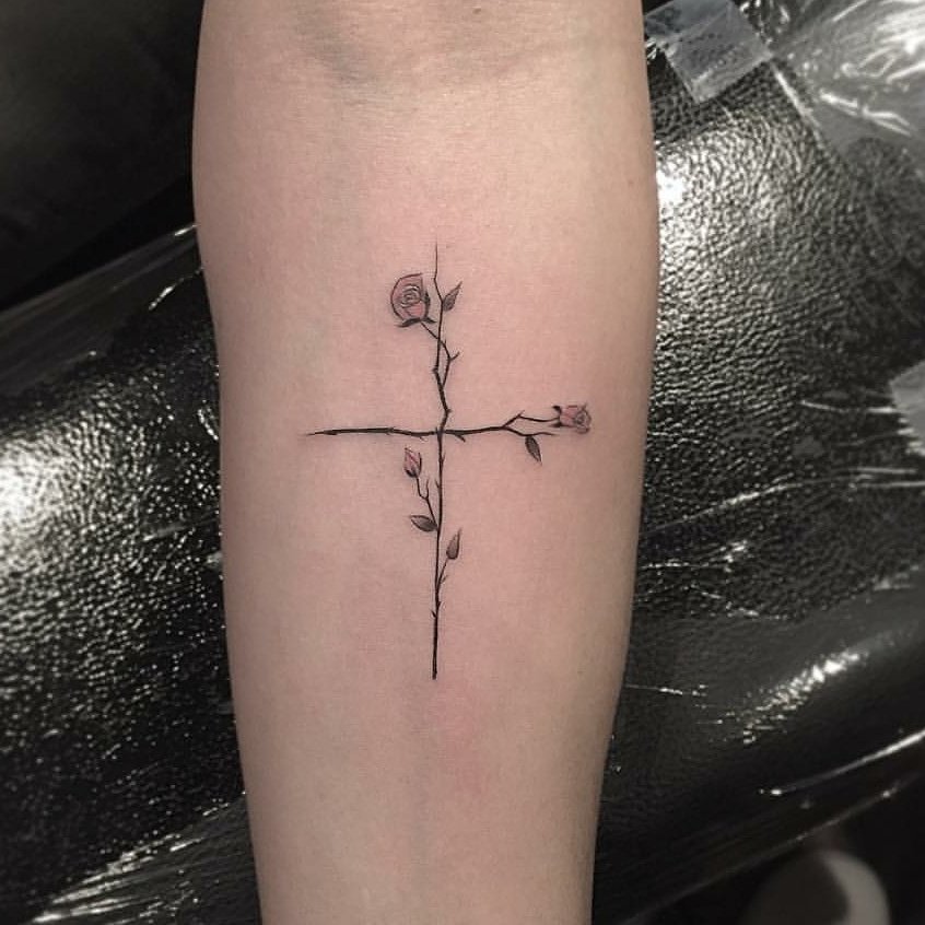 Tattoo of a cross made of intertwined branches and roses on a forearm.