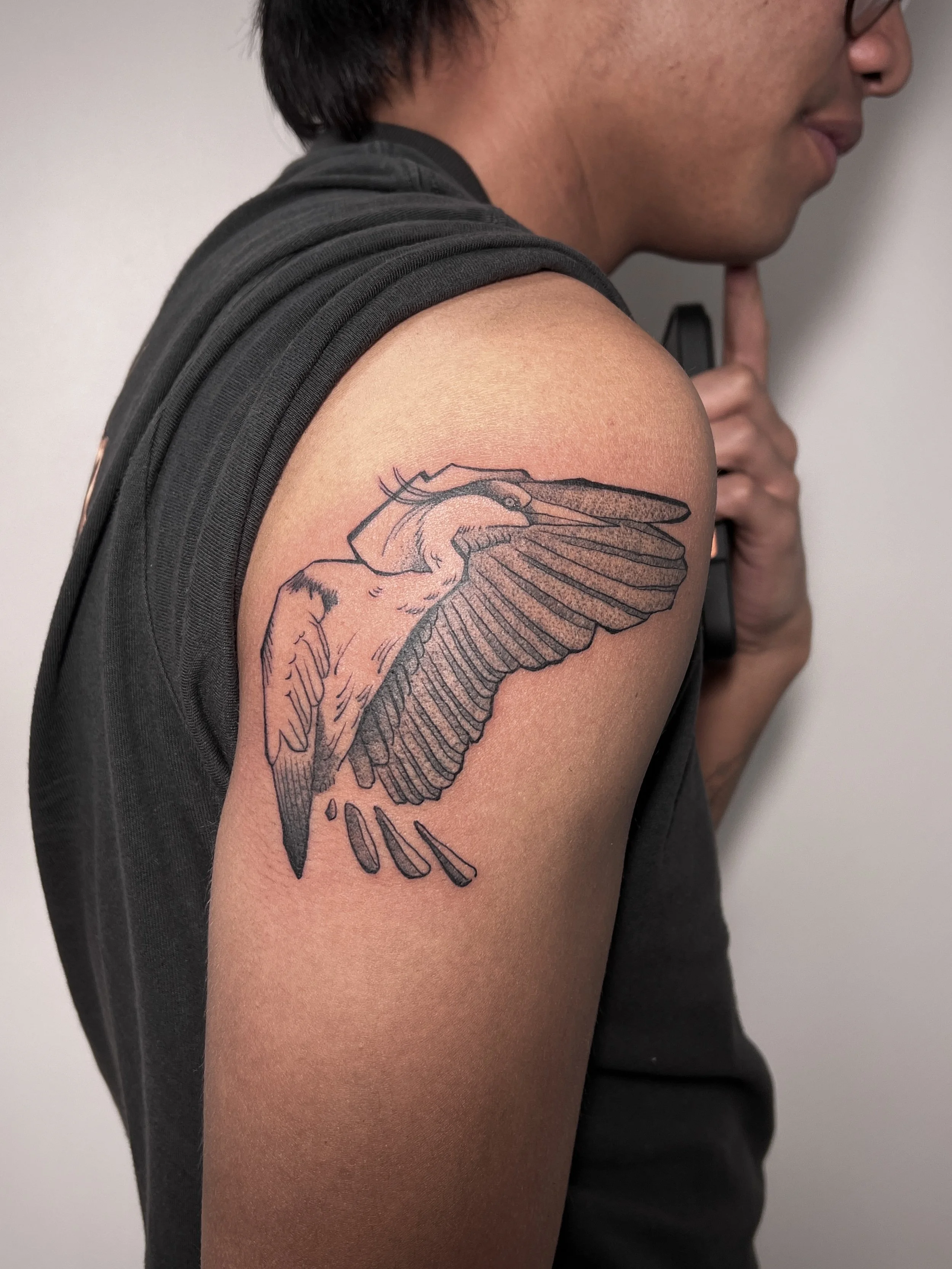 A person wearing a black sleeveless shirt with a tattoo of a flying bird on the upper arm.
