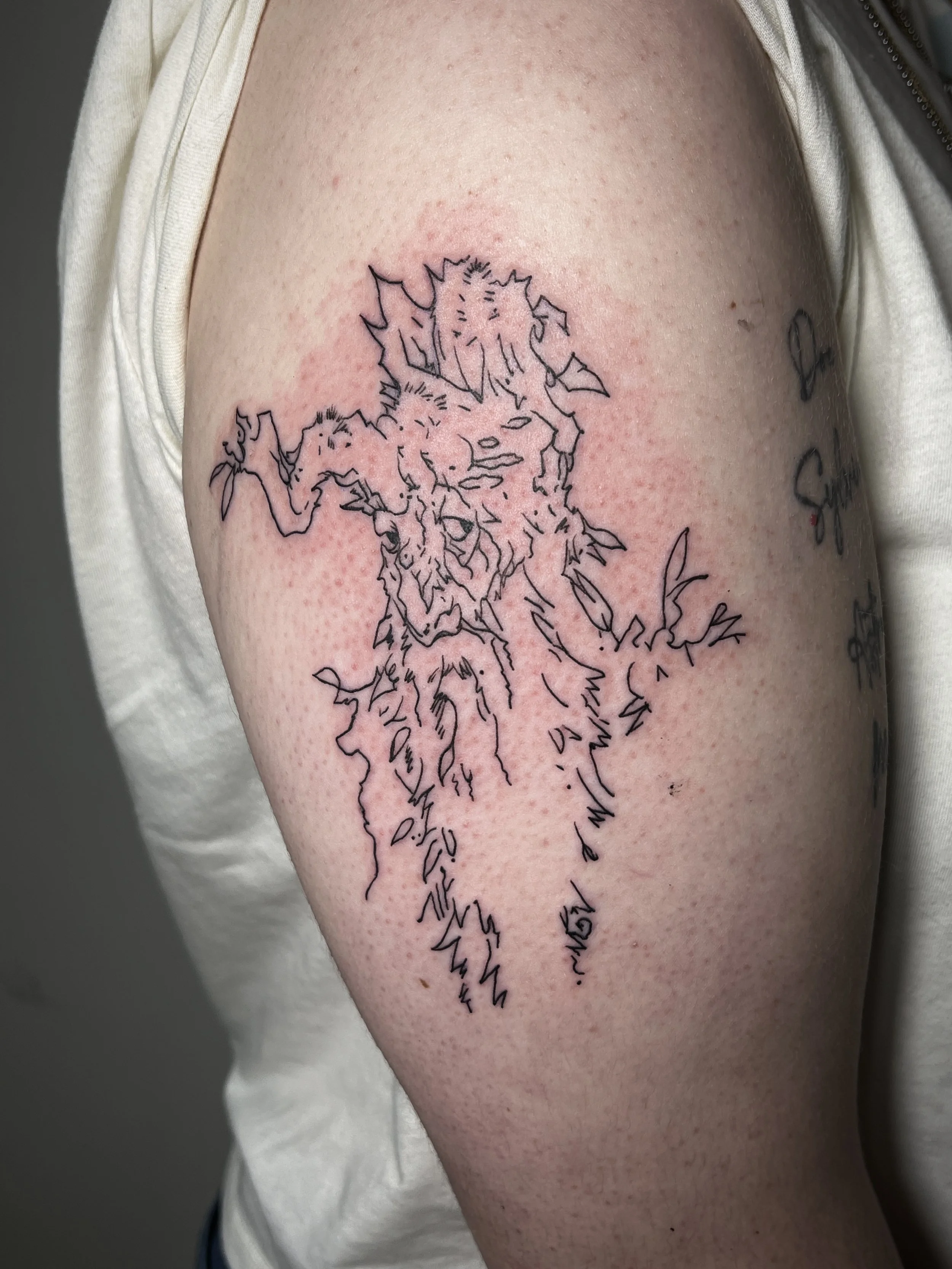 A tattoo of an outline of a wolf on a person's upper arm, with some writing underneath
