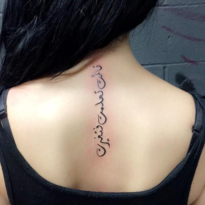 Person with a tattoo in Arabic script on their upper back, wearing a black top.