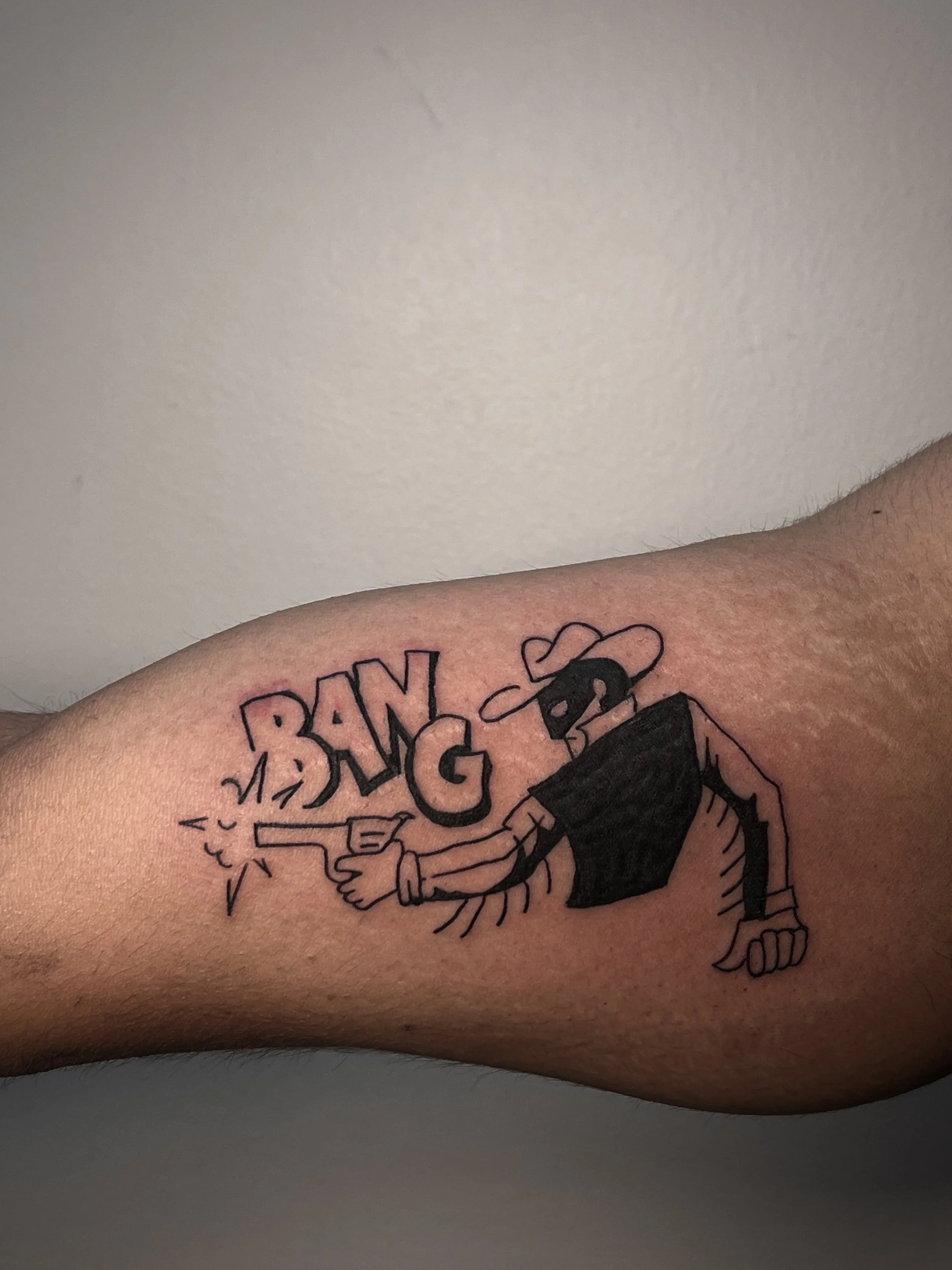 Tattoo of a cowboy shooting a pistol, with the word BANG in the background.