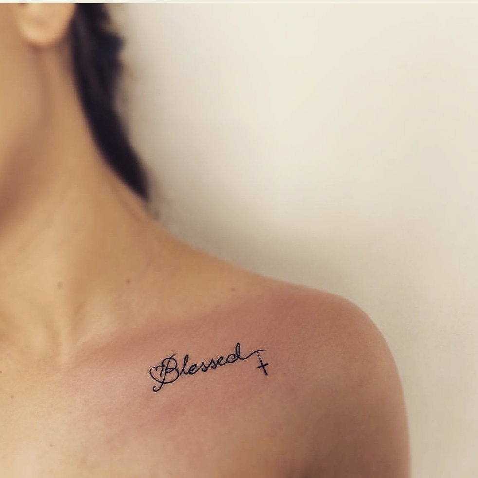 Tattoo of the word Blessed with a cross on a person's shoulder