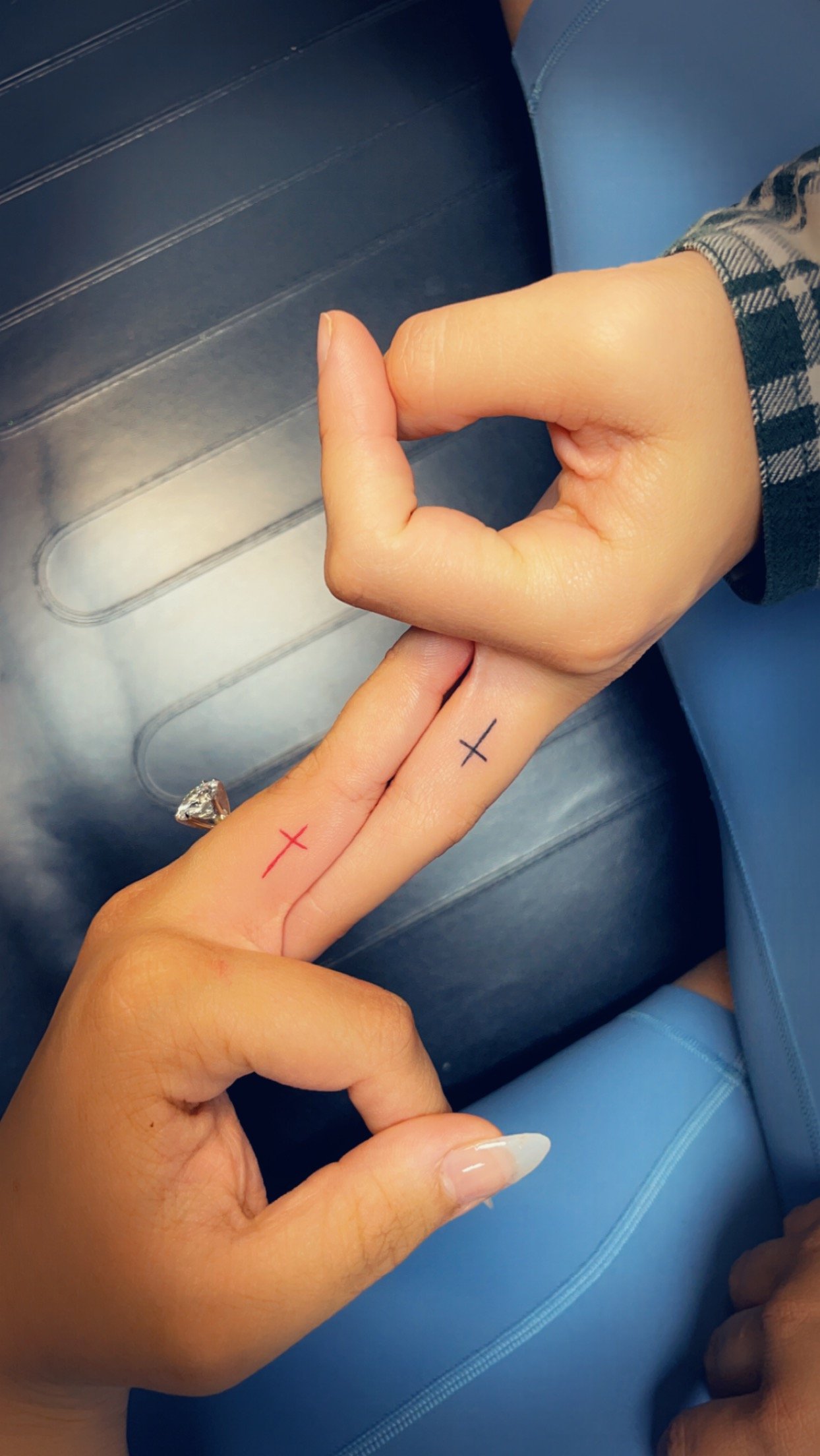 Two hands touching fingers with small cross tattoos, one red and one black, against a dark background.