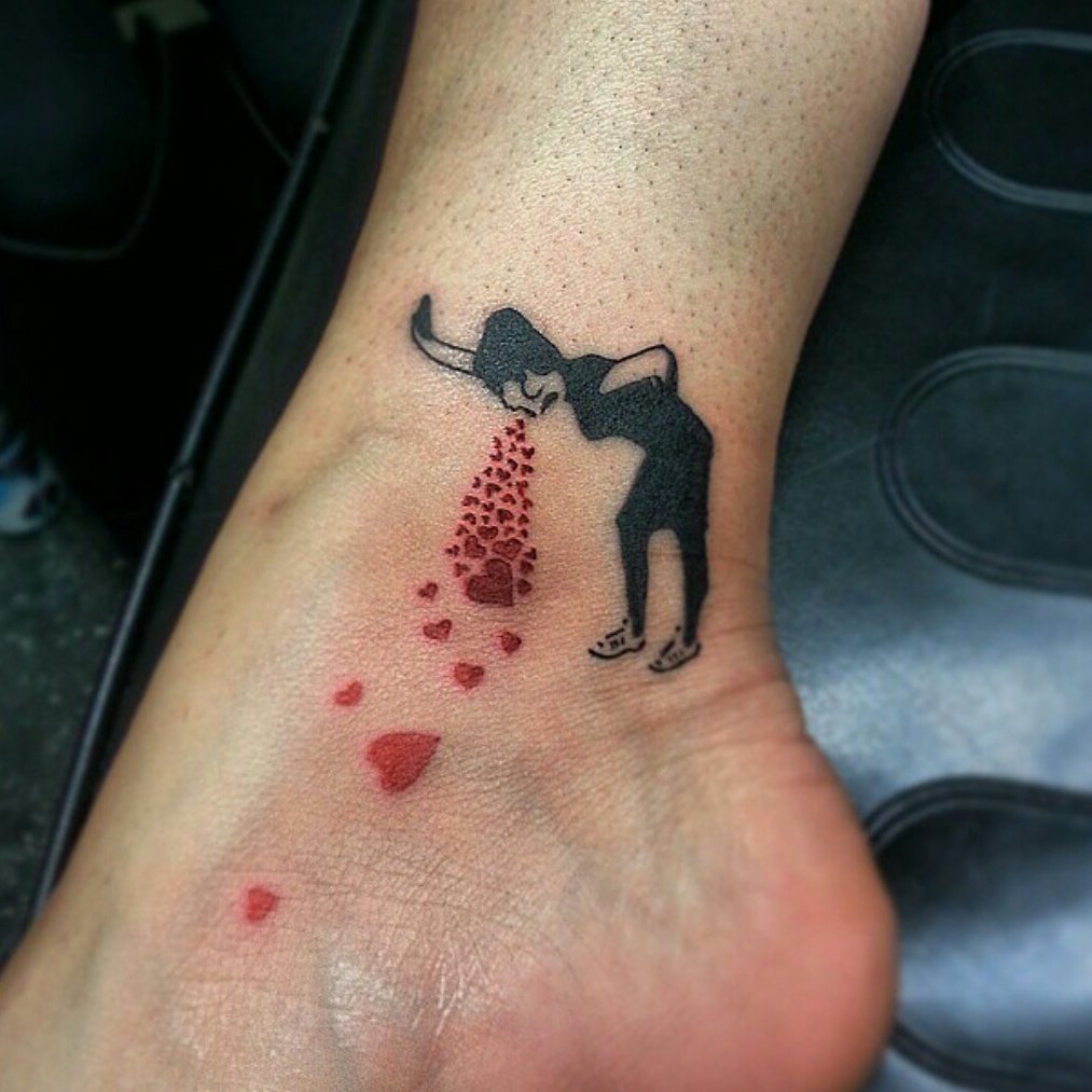 Tattoo of a figure vomiting red hearts on a foot