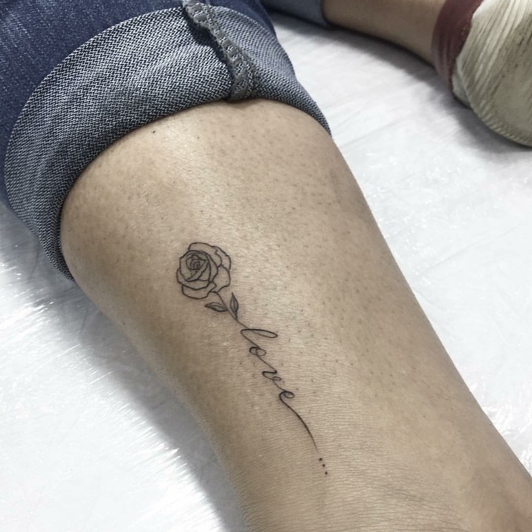 Close-up of a leg with a tattoo of a rose and the word "love" in cursive.
