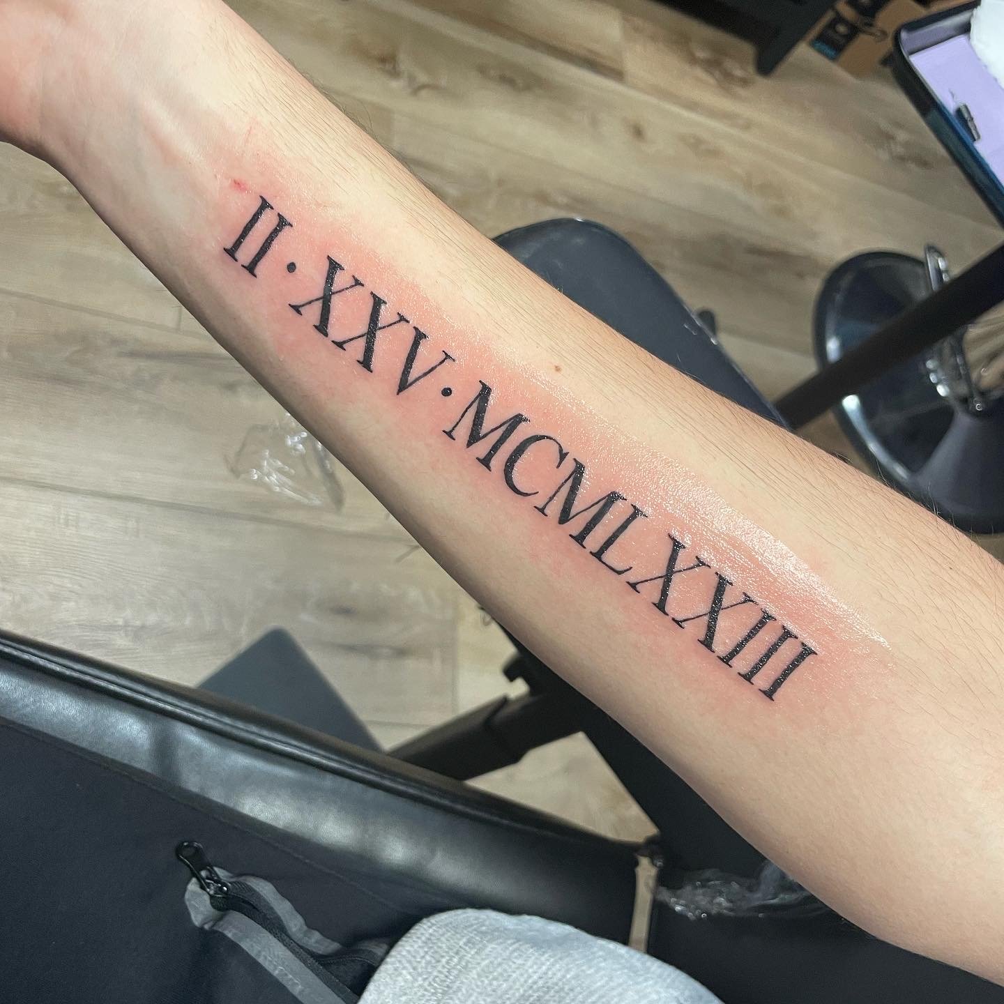 Forearm tattoo with Roman numerals II, XXV, MCMLXXIII.