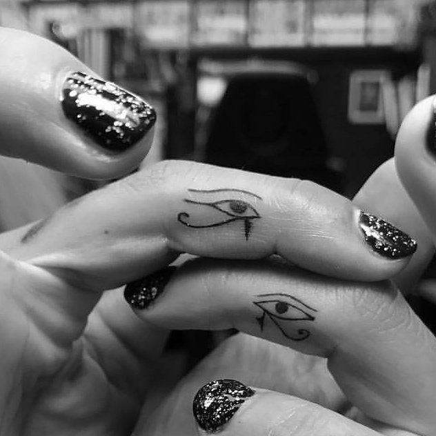 Fingers with Eye of Horus tattoos and glittery black nail polish.