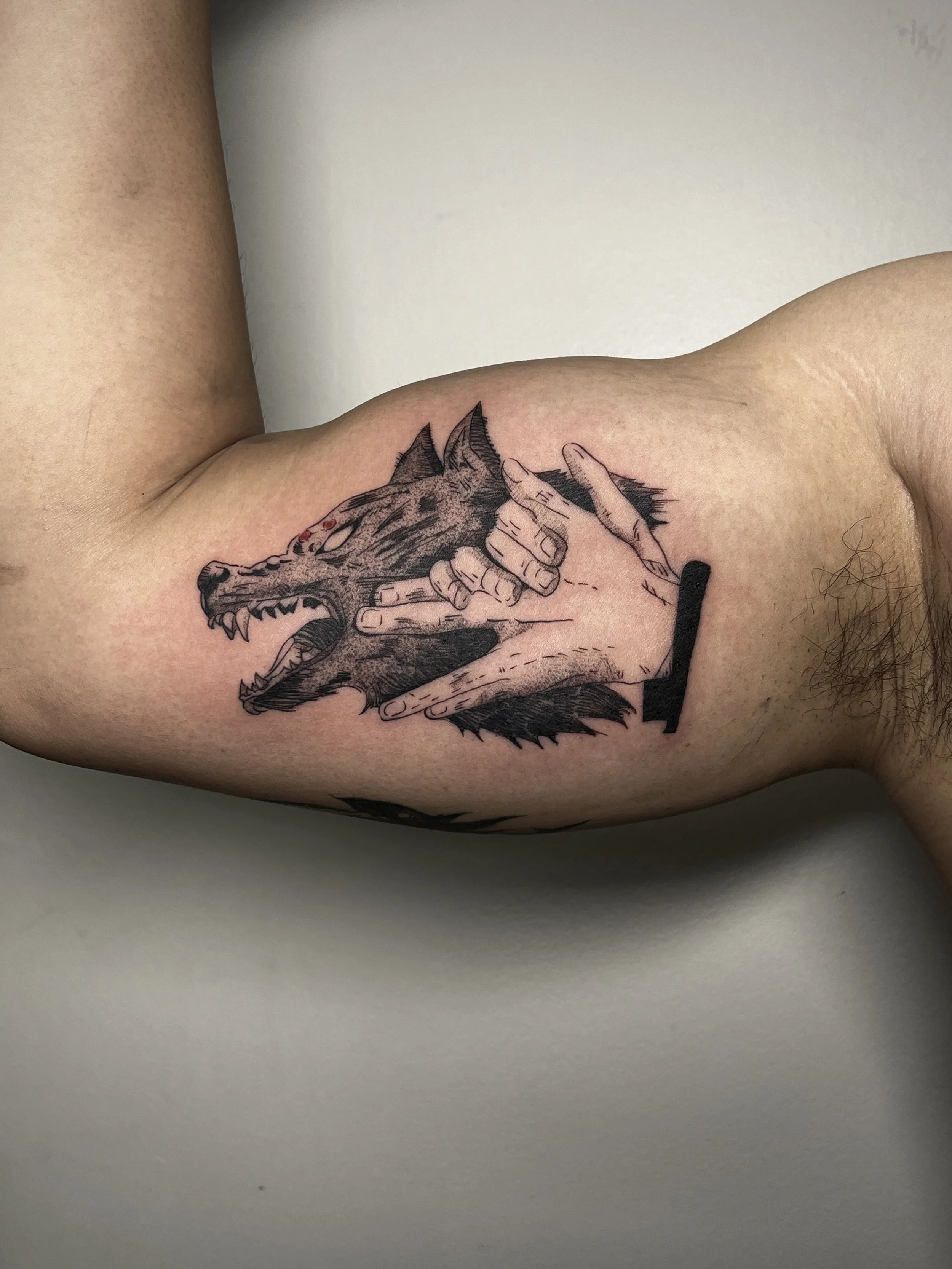 Tattoo of a wolf's head with an open mouth, snarling, and a human hand holding a cigarette near its head.