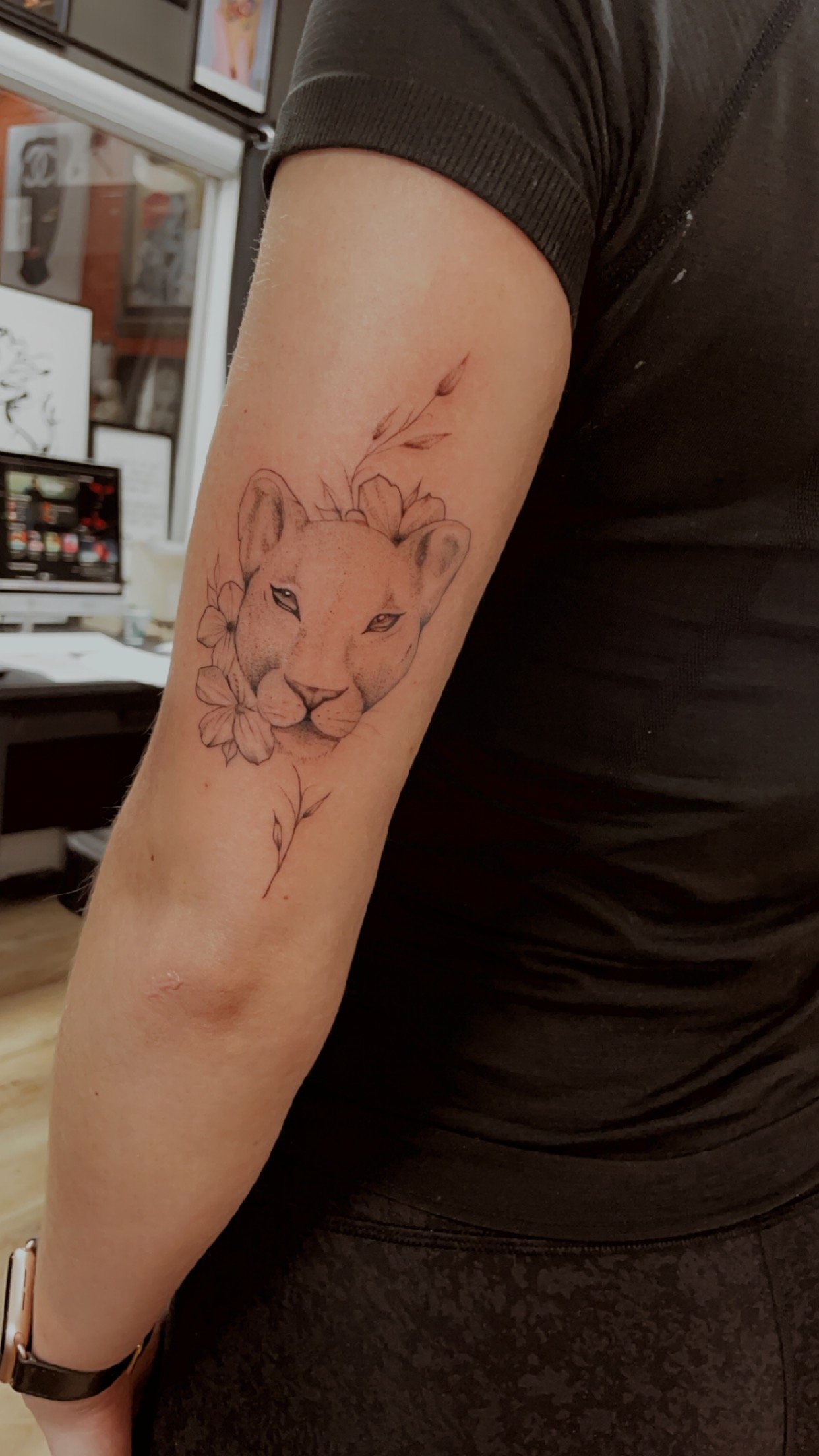 A lioness tattoo with flowers on a person's arm.
