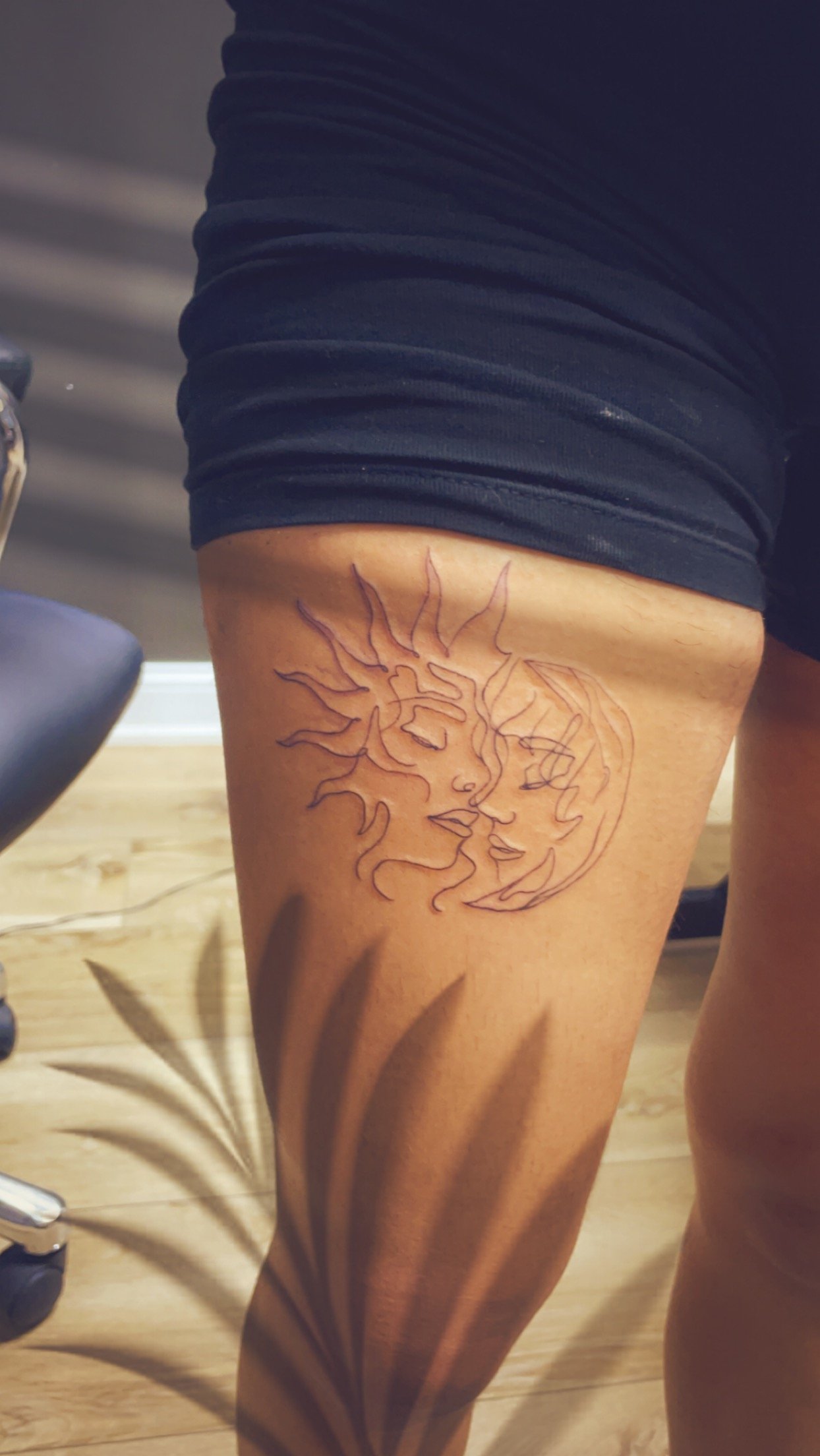 Tattoo of a sun and moon on a person's thigh, featuring abstract faces.